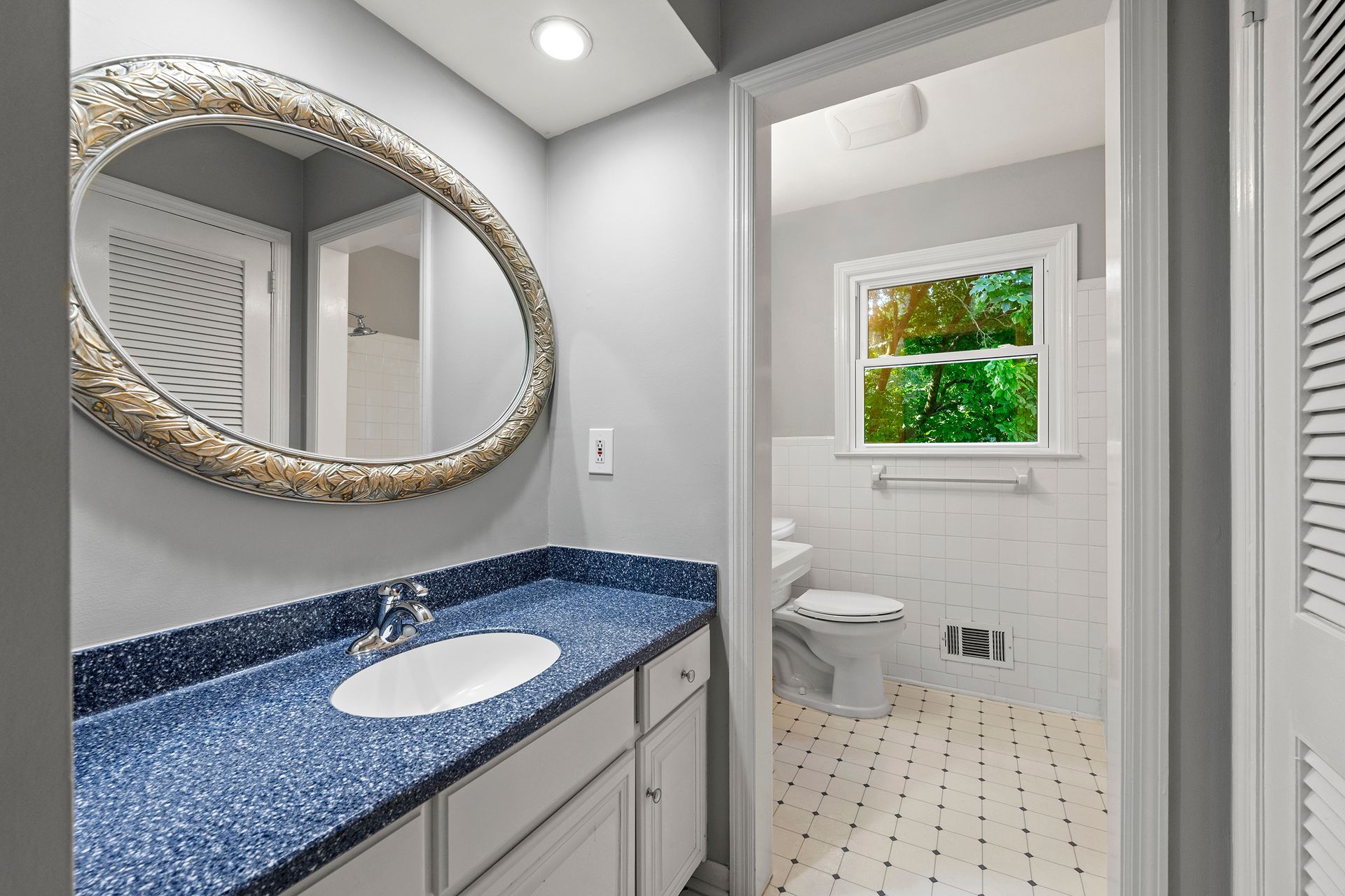 A bathroom with a sink , mirror , toilet and window.