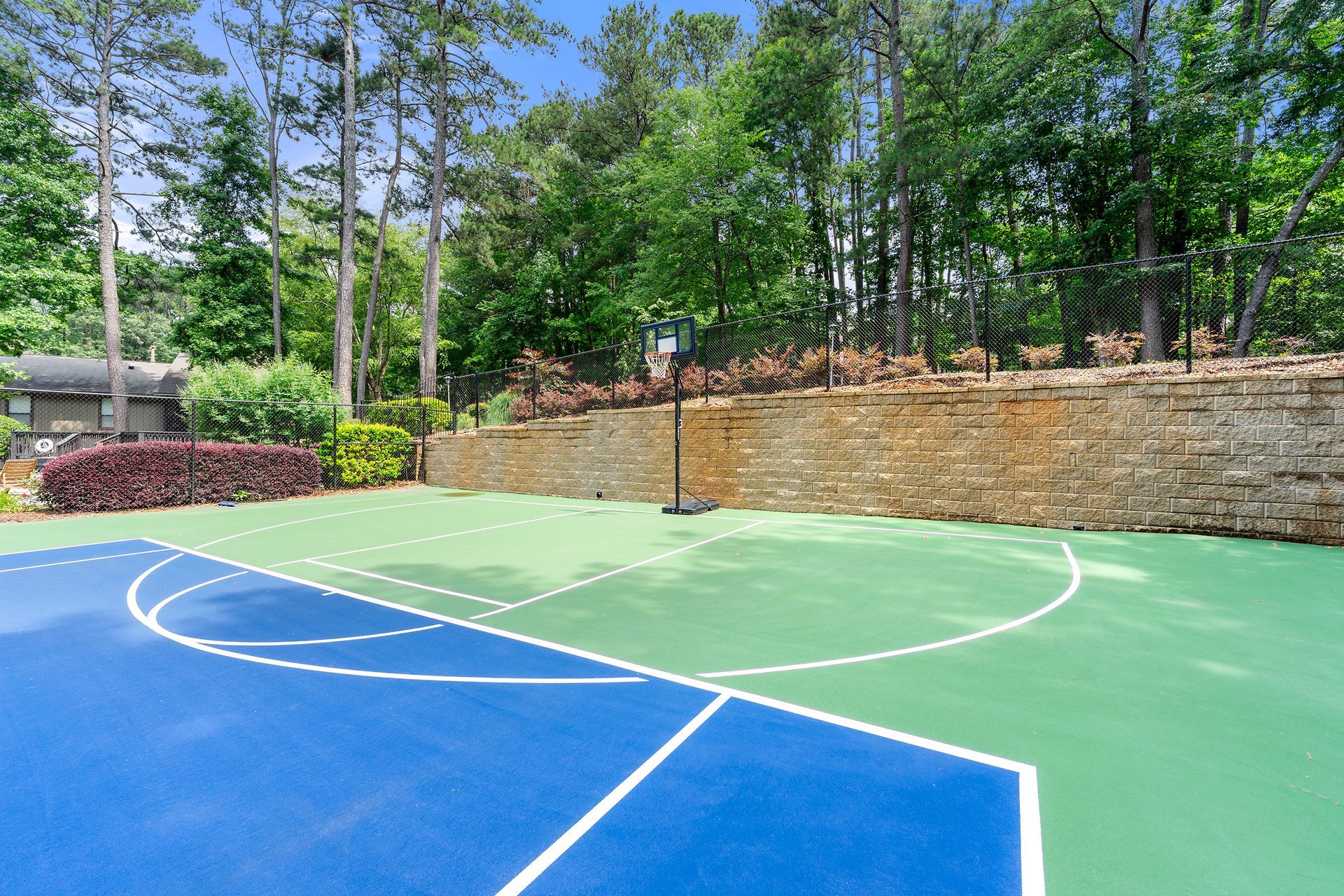 A blue and green basketball court with trees in the background.