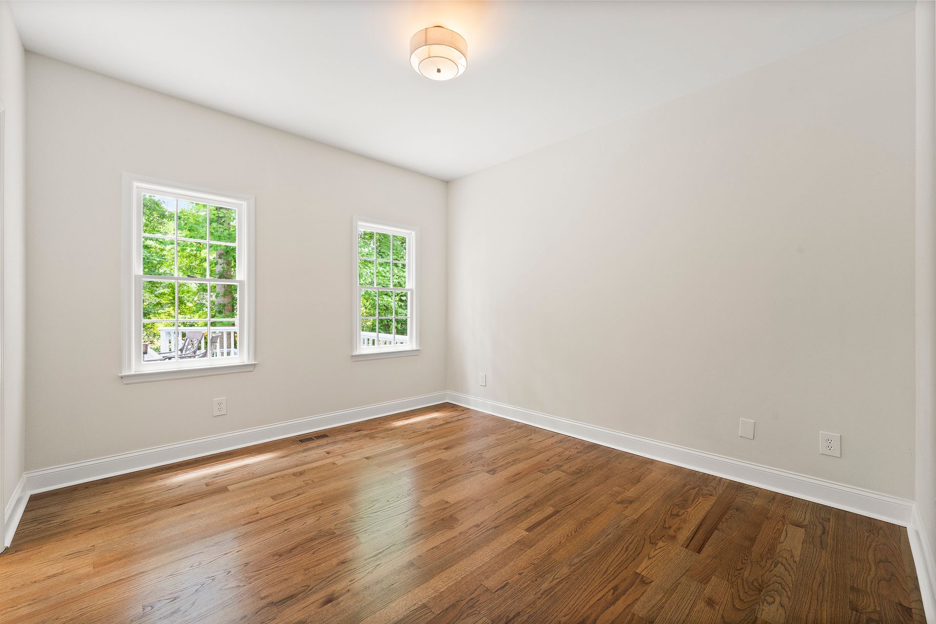 An empty room with hardwood floors and two windows