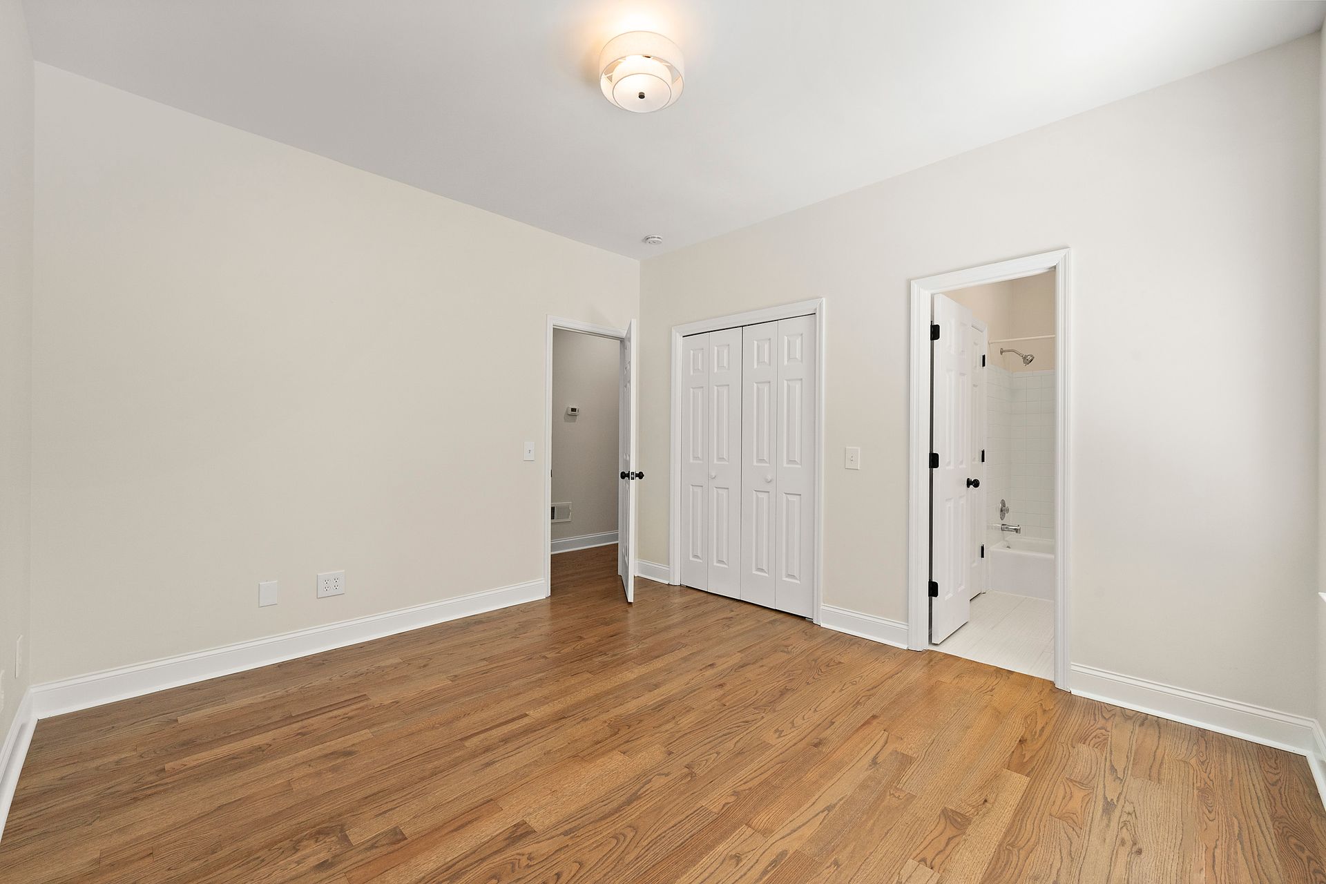 An empty bedroom with hardwood floors and white walls.