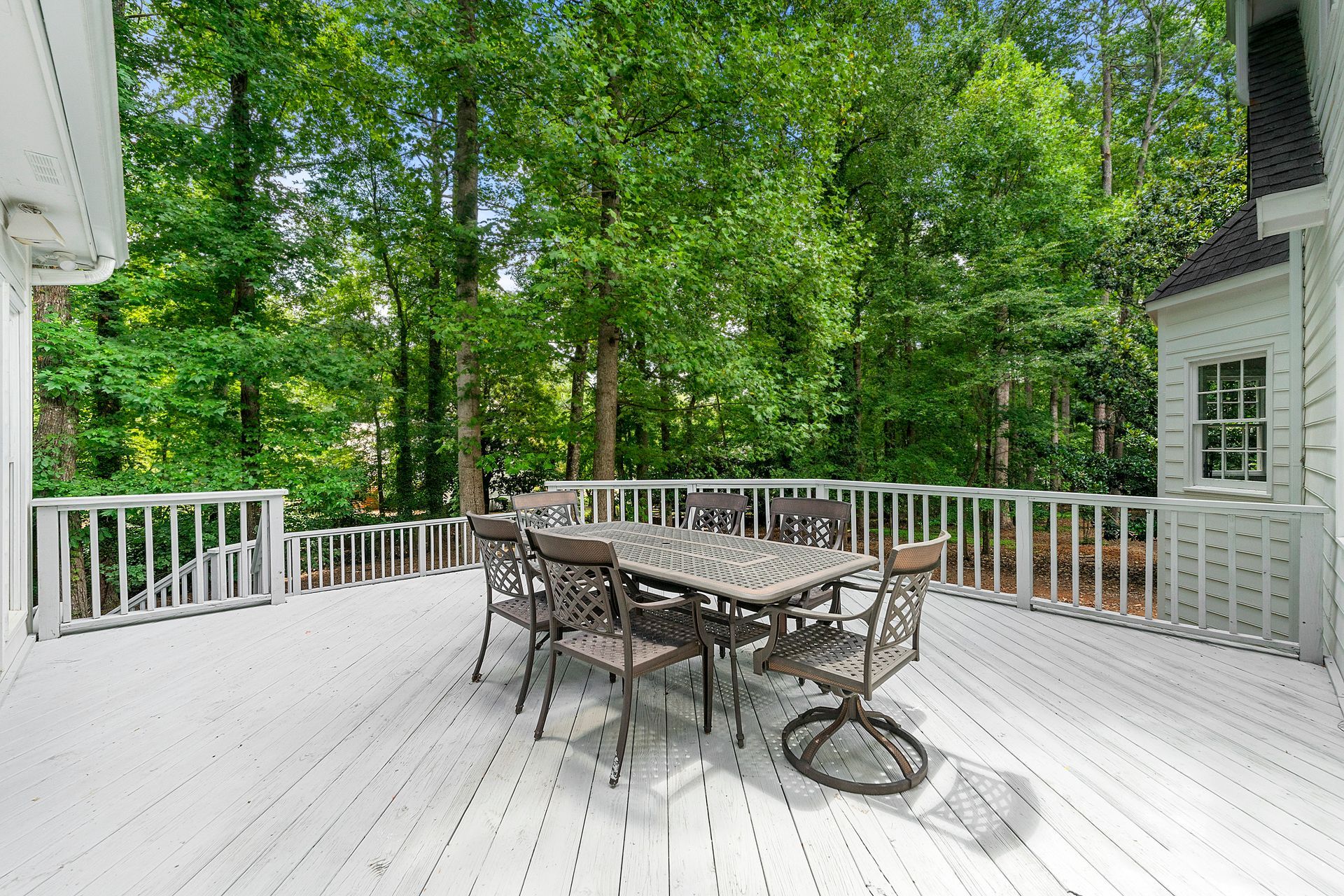 A large white deck with a table and chairs on it surrounded by trees.