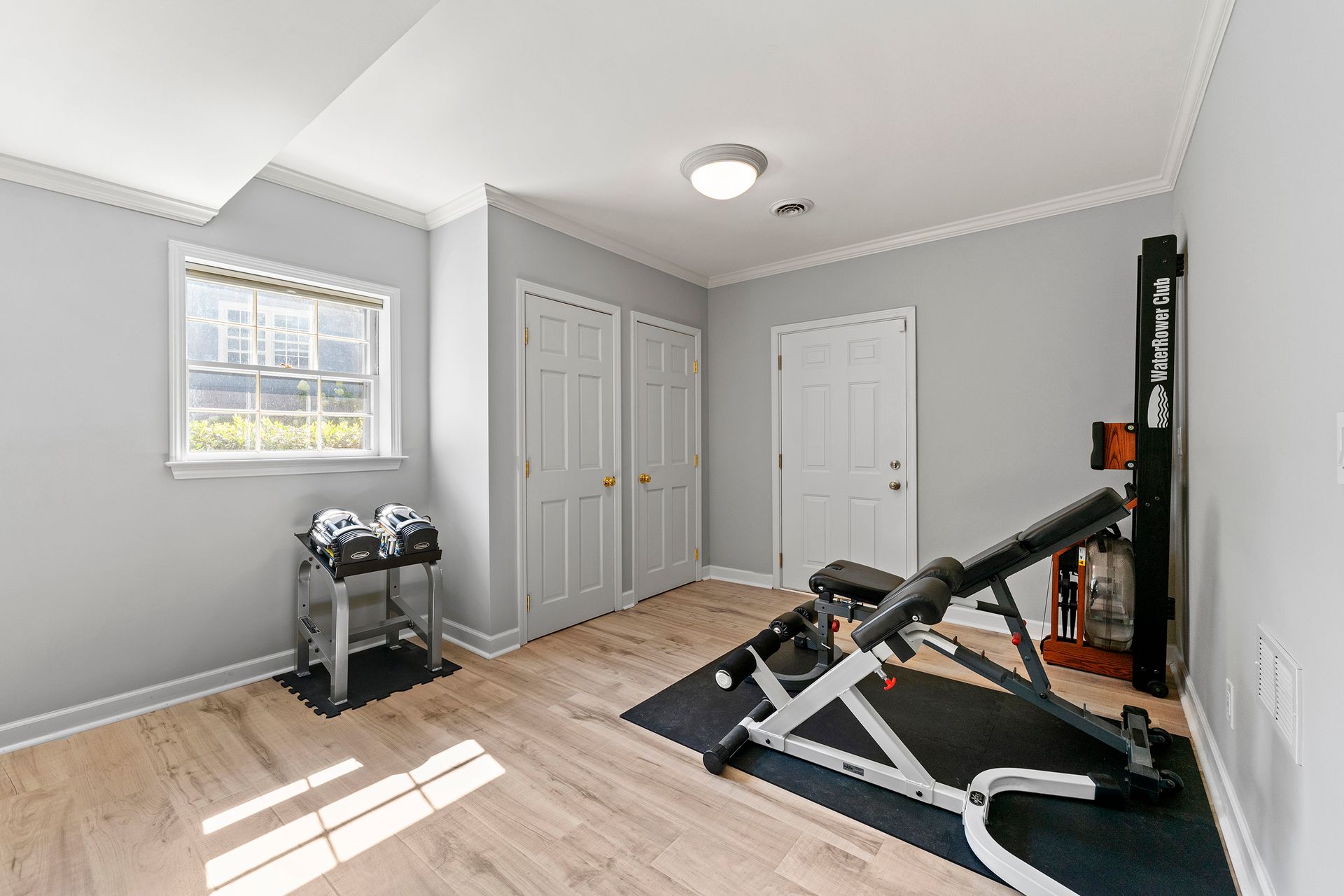 A home gym with a bench , dumbbells , and a rowing machine.