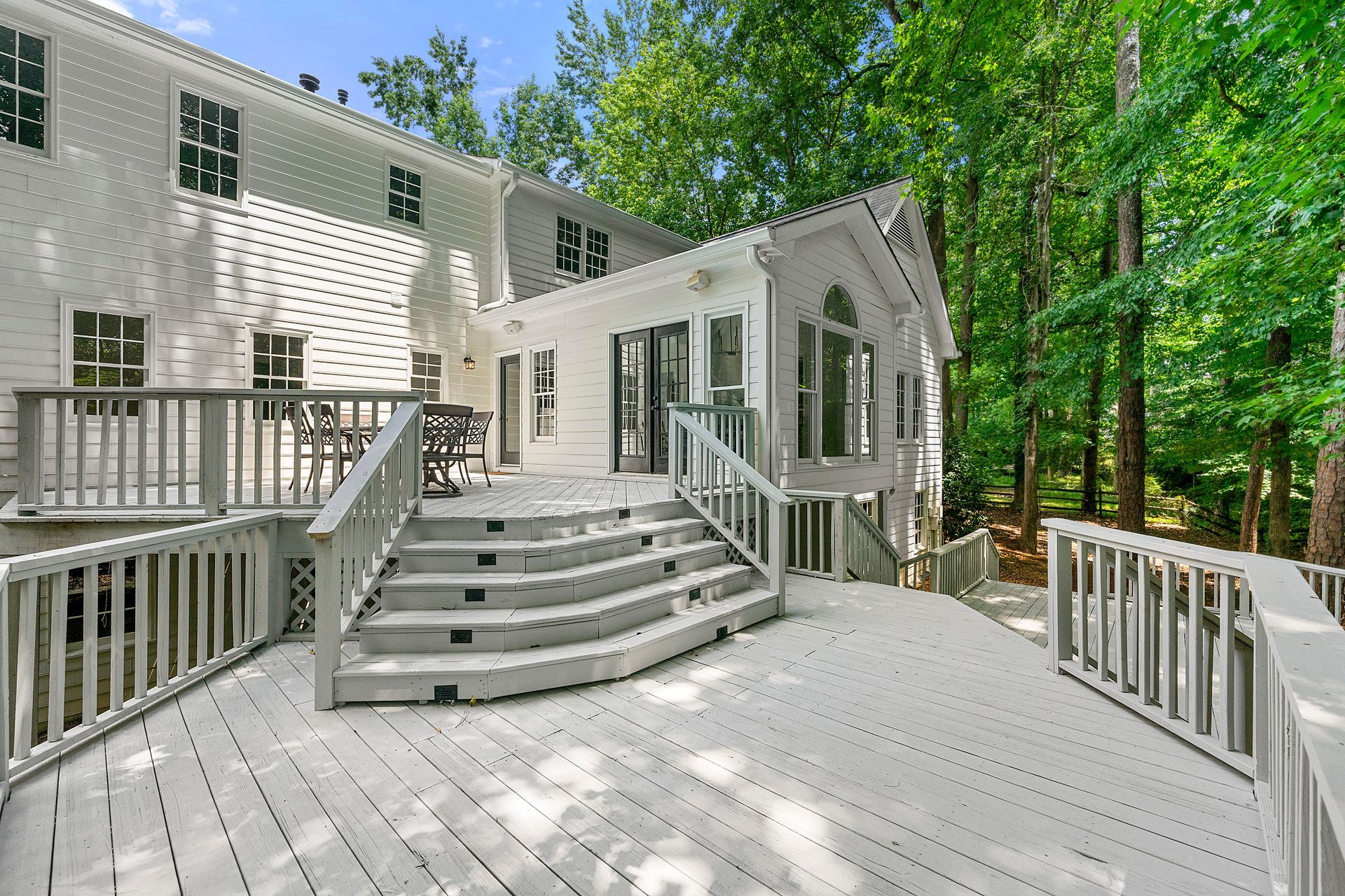 A large white house with a large deck and stairs leading up to it.