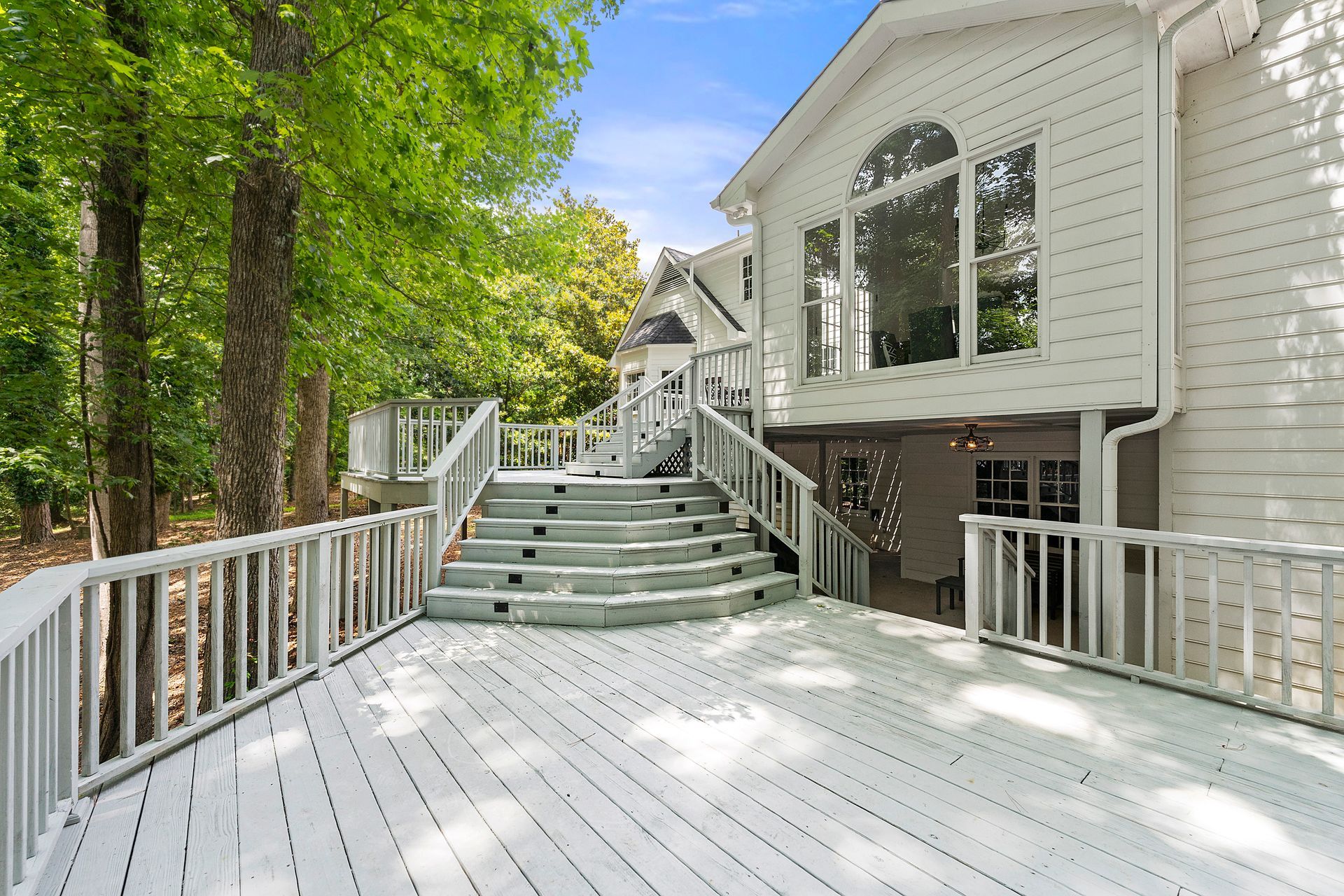 A large white house with a large deck and stairs leading up to it.