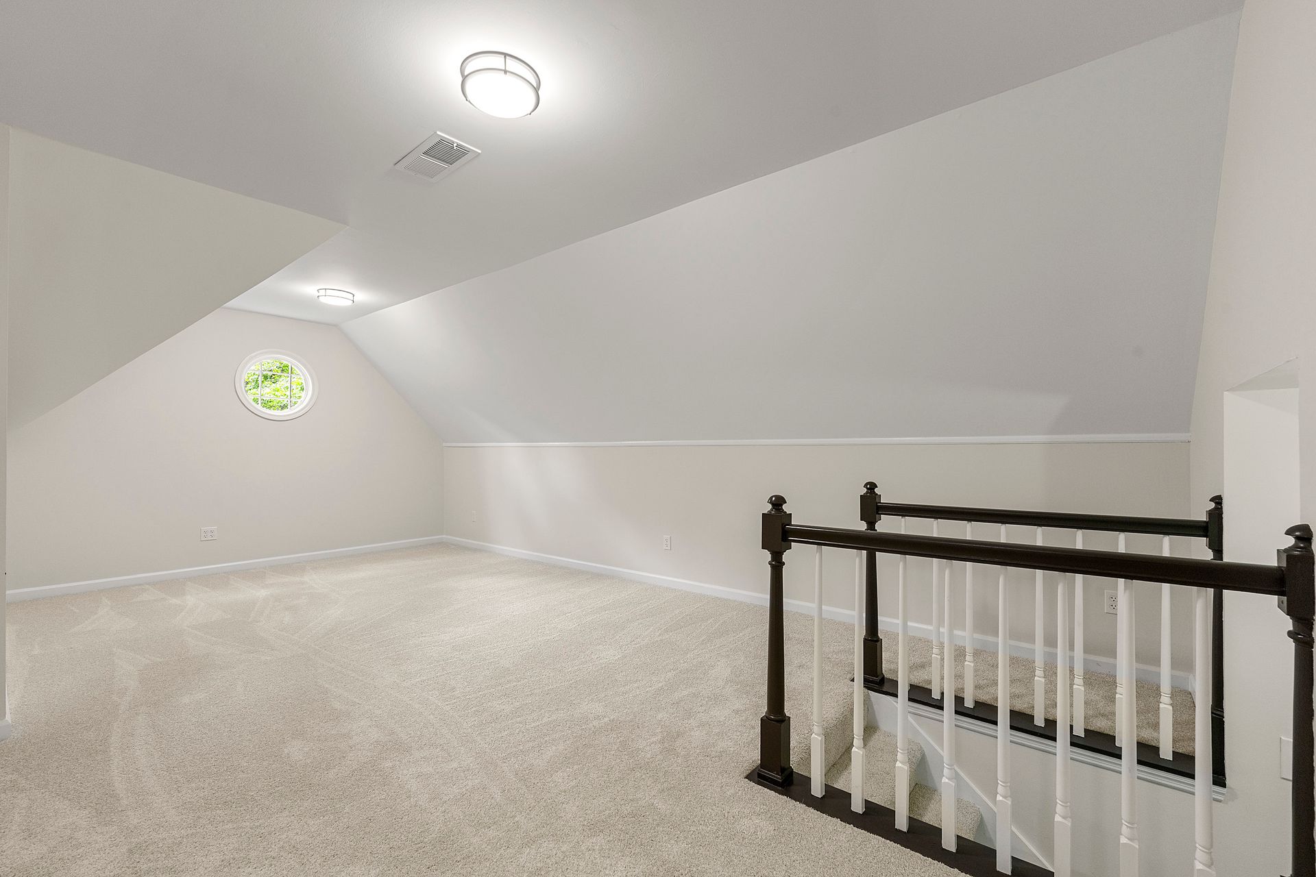 An empty attic with a staircase and a window.