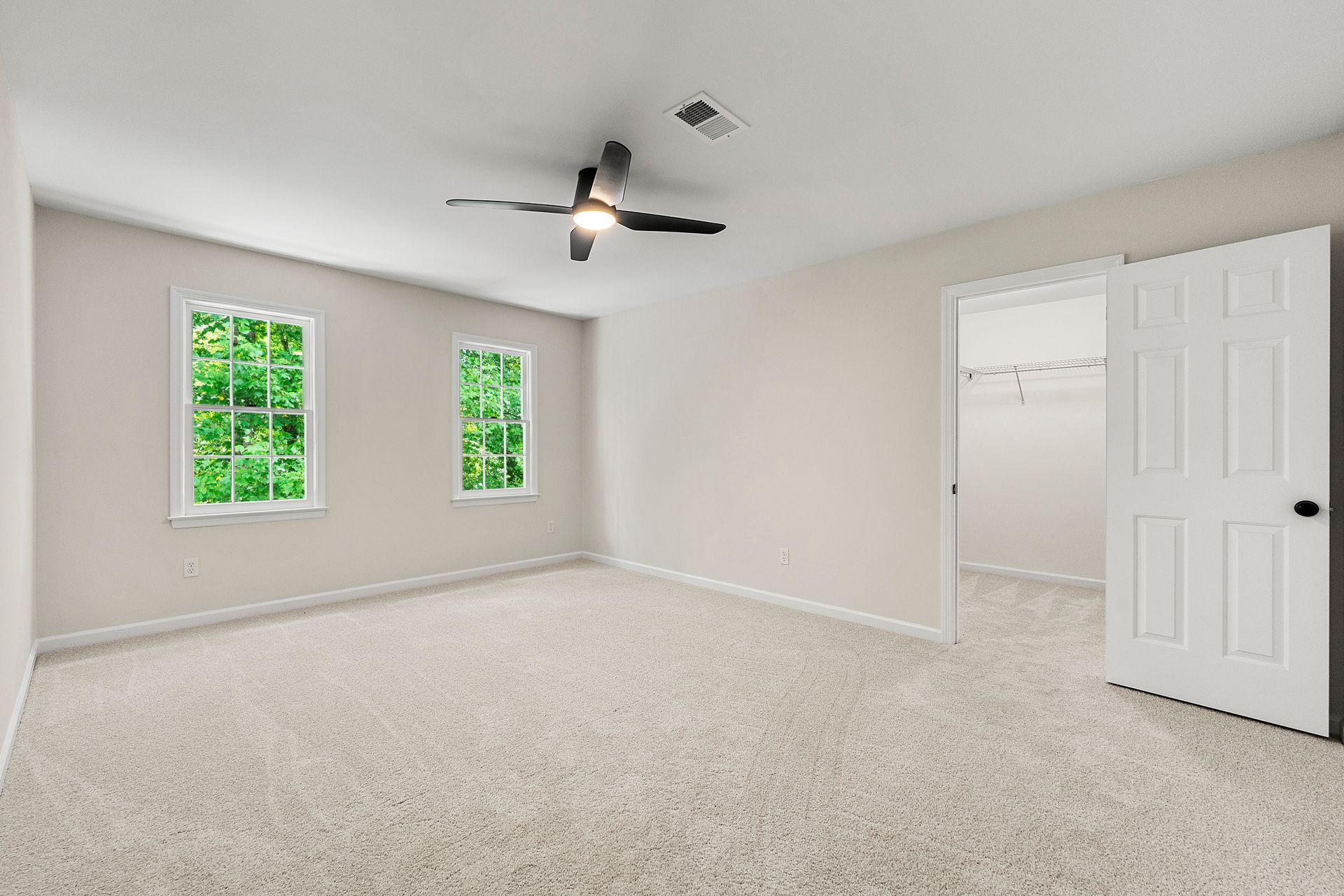 An empty bedroom with a ceiling fan and two windows.