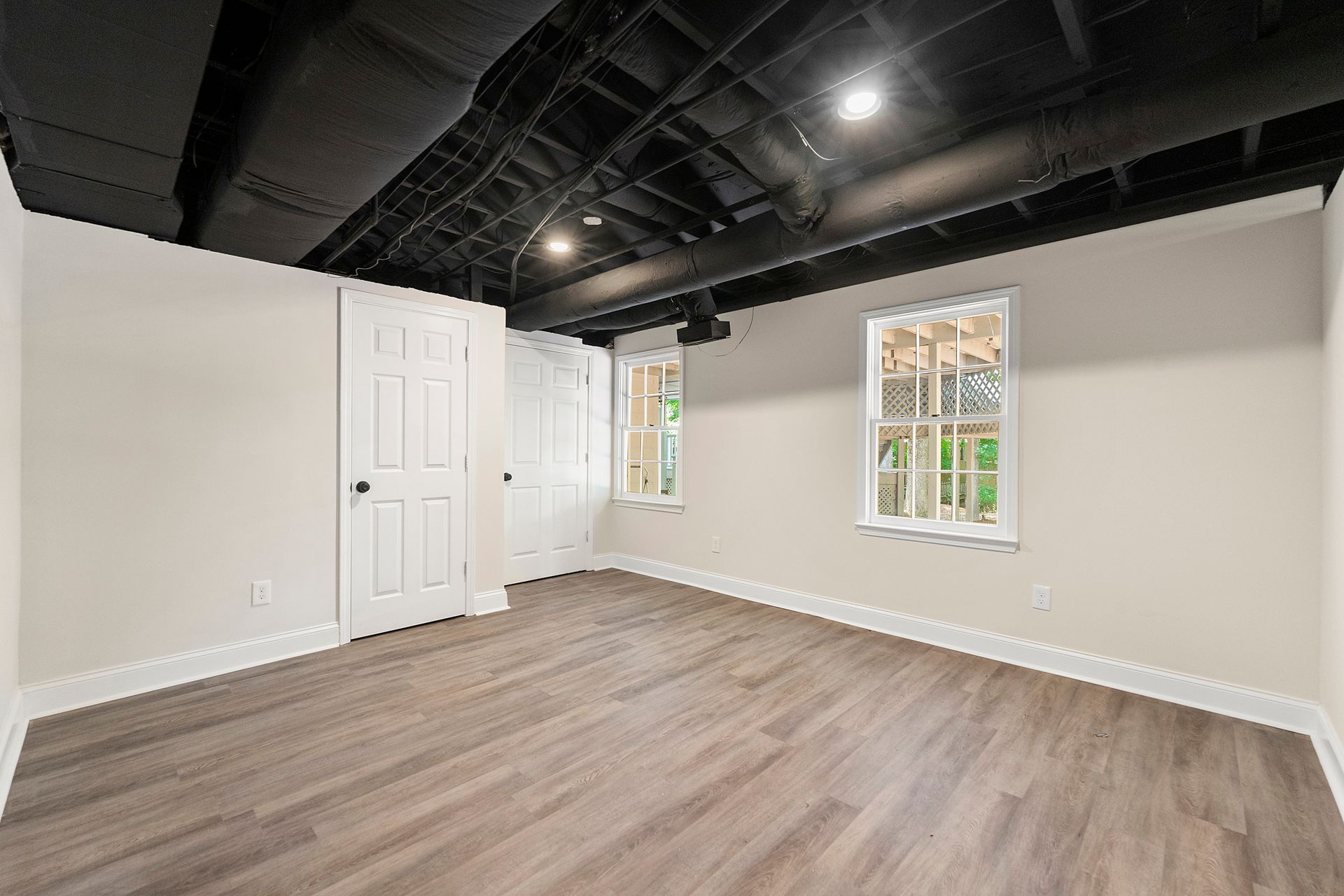 An empty basement with hardwood floors and two windows.