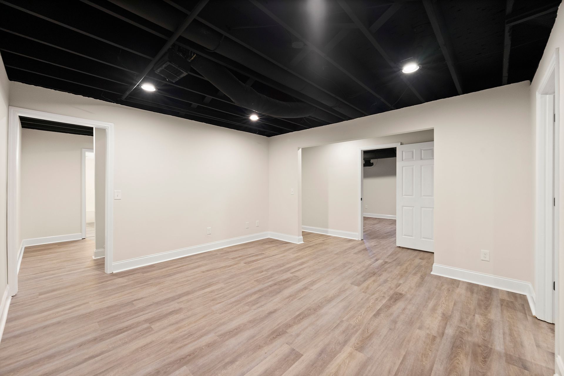 An empty basement with hardwood floors and a black ceiling.