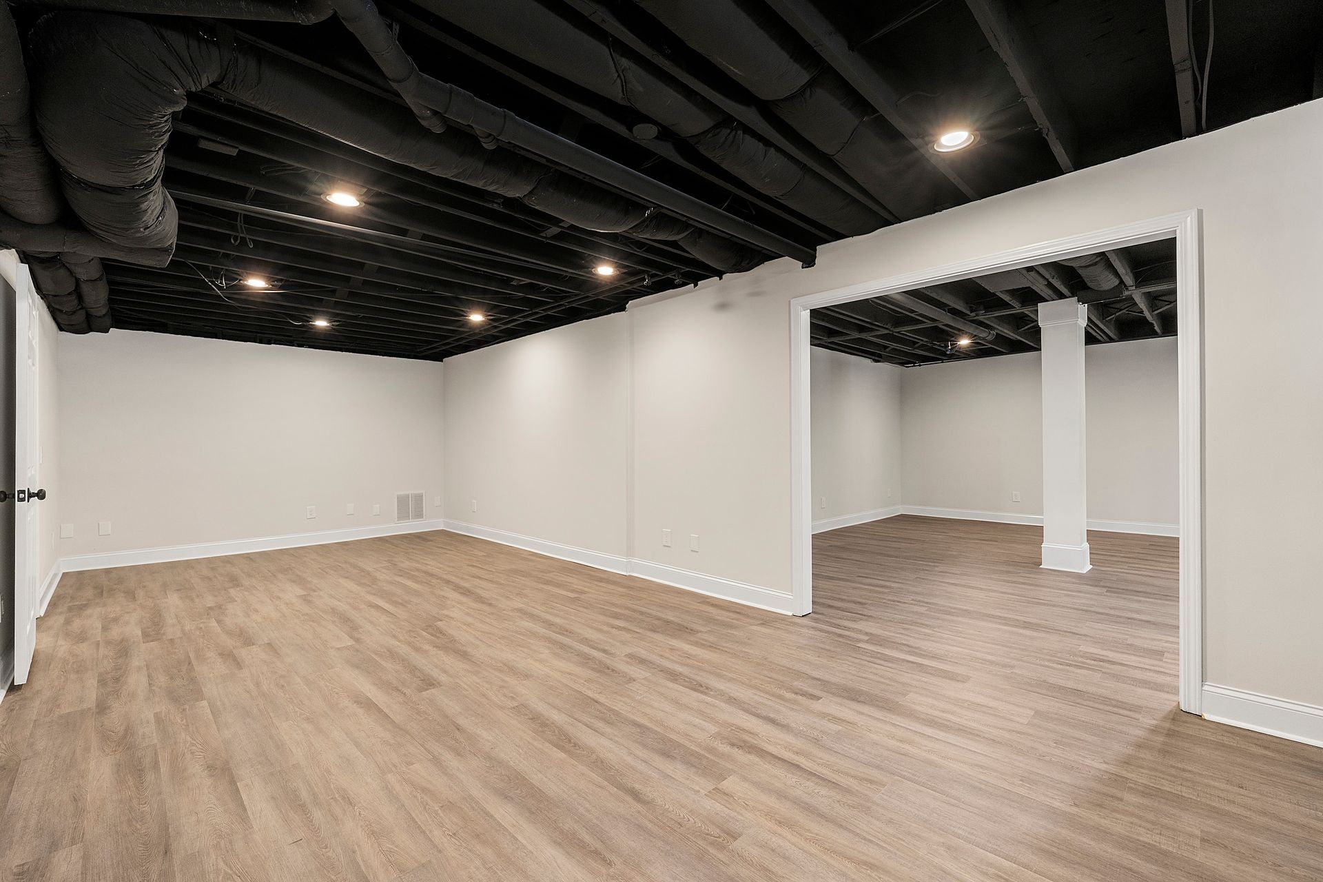 An empty basement with wooden floors and white walls.
