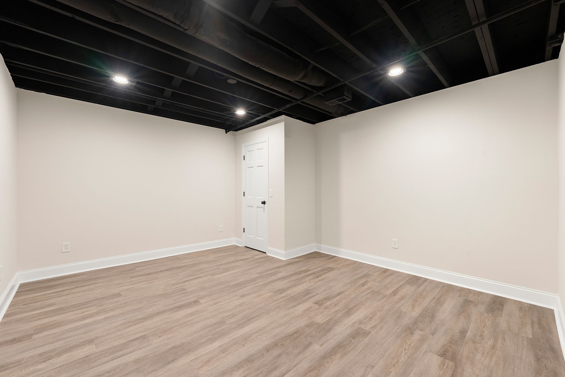 An empty basement with hardwood floors and white walls.