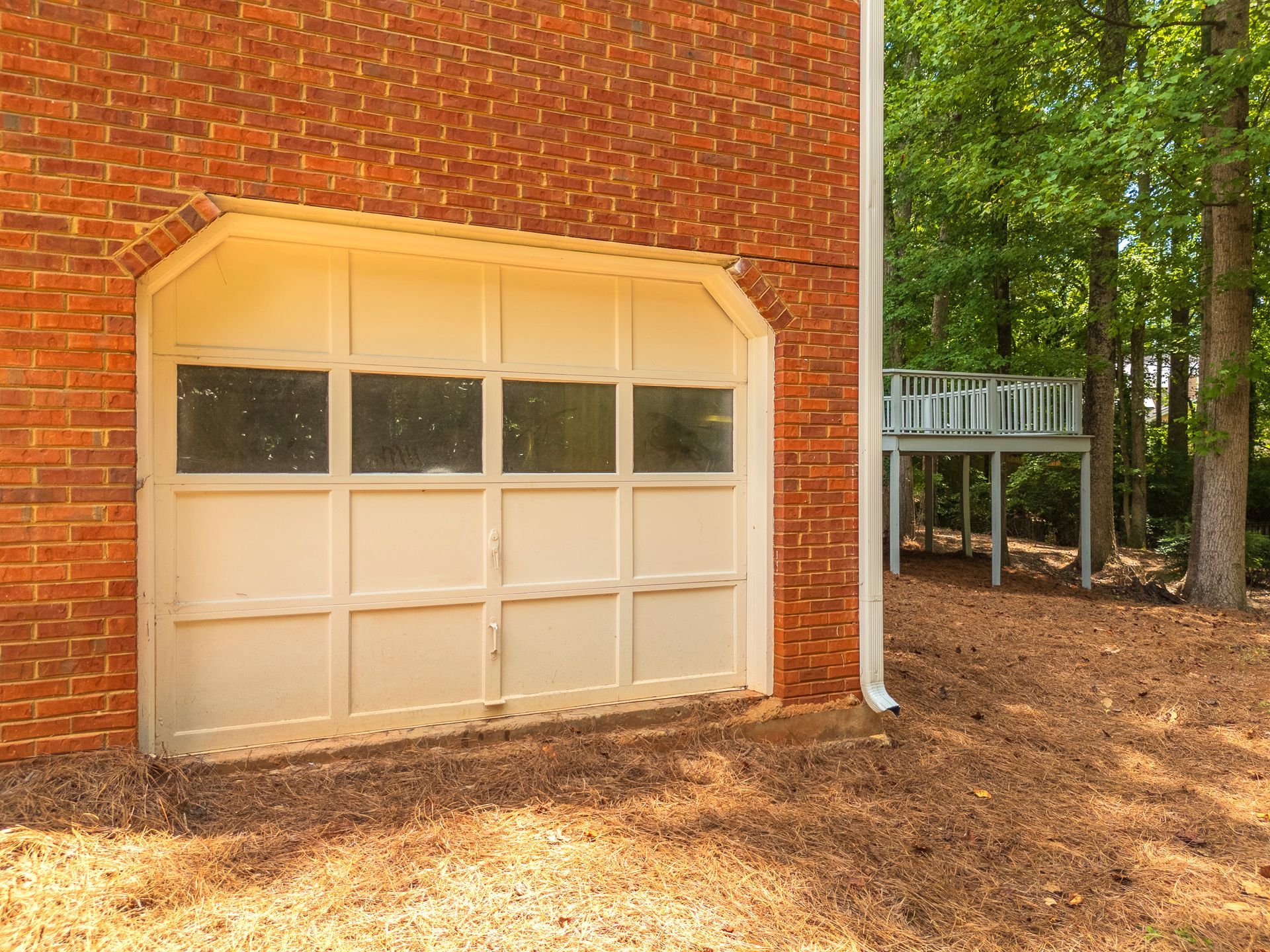 A white garage door is on the side of a red brick house.
