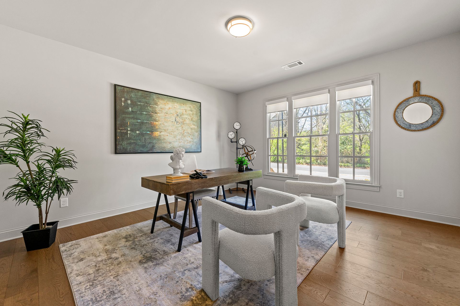 A living room with two chairs , a desk , and a painting on the wall.