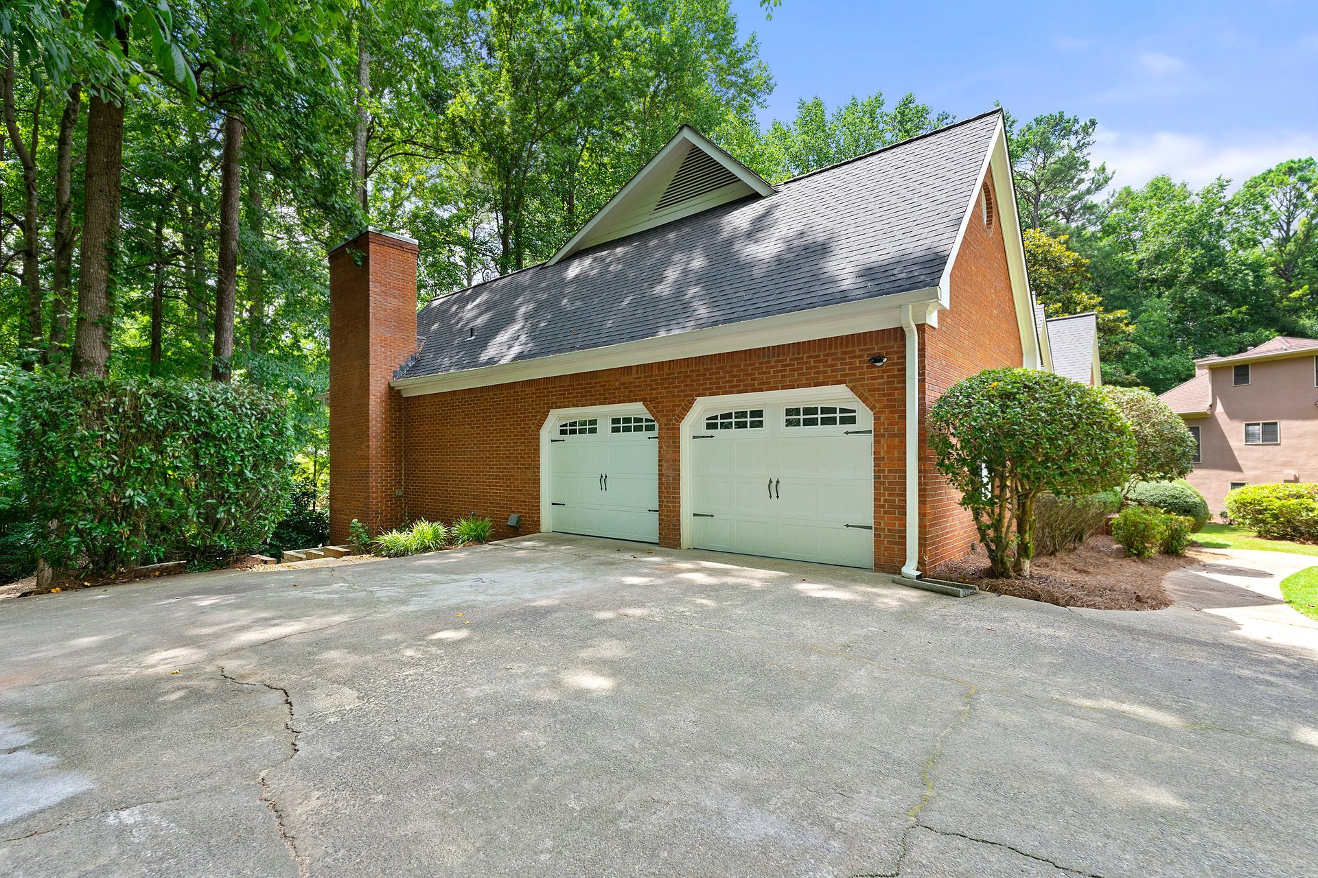 A large brick garage with two white garage doors is surrounded by trees.