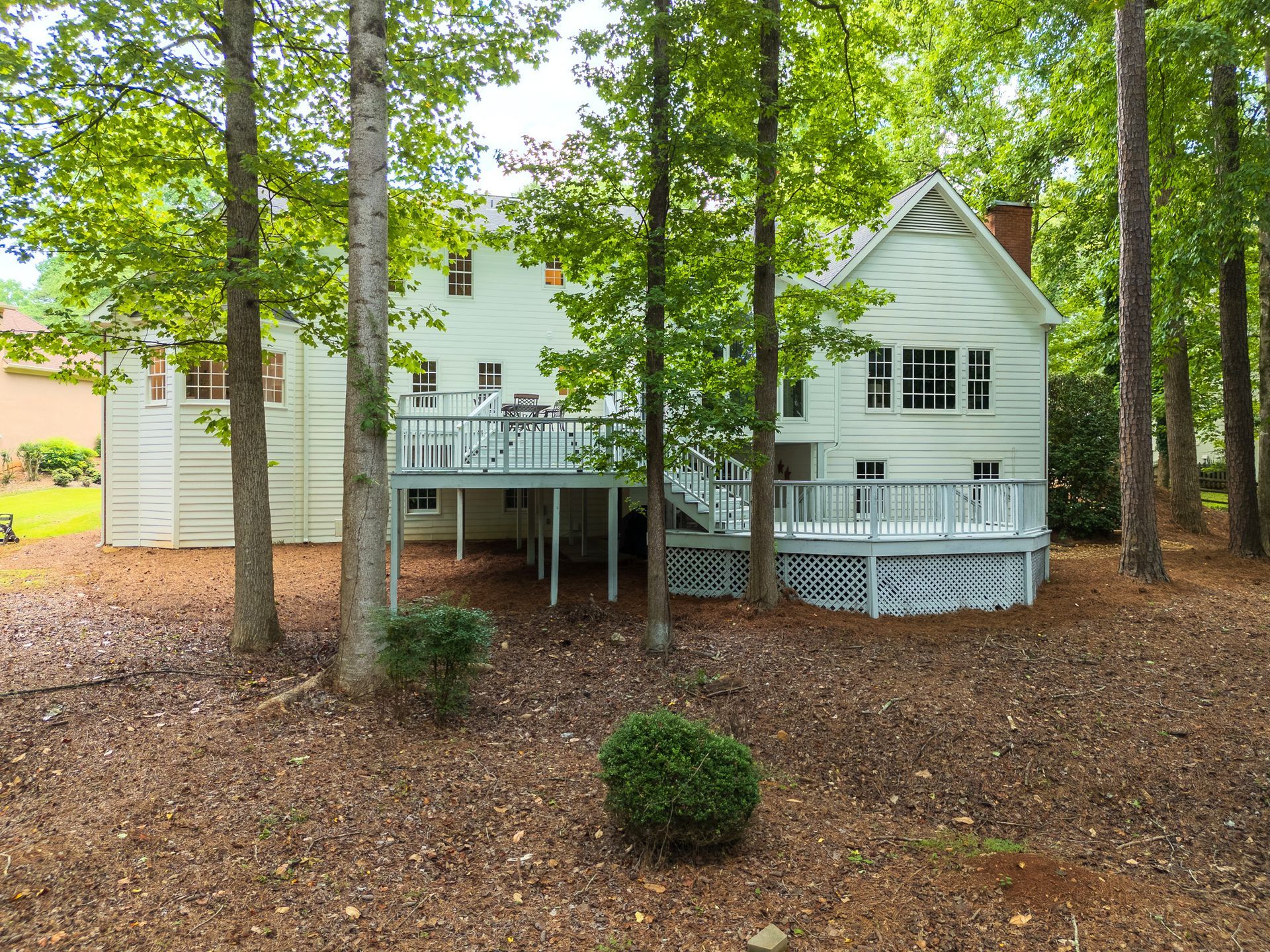 A white house with a large deck is surrounded by trees