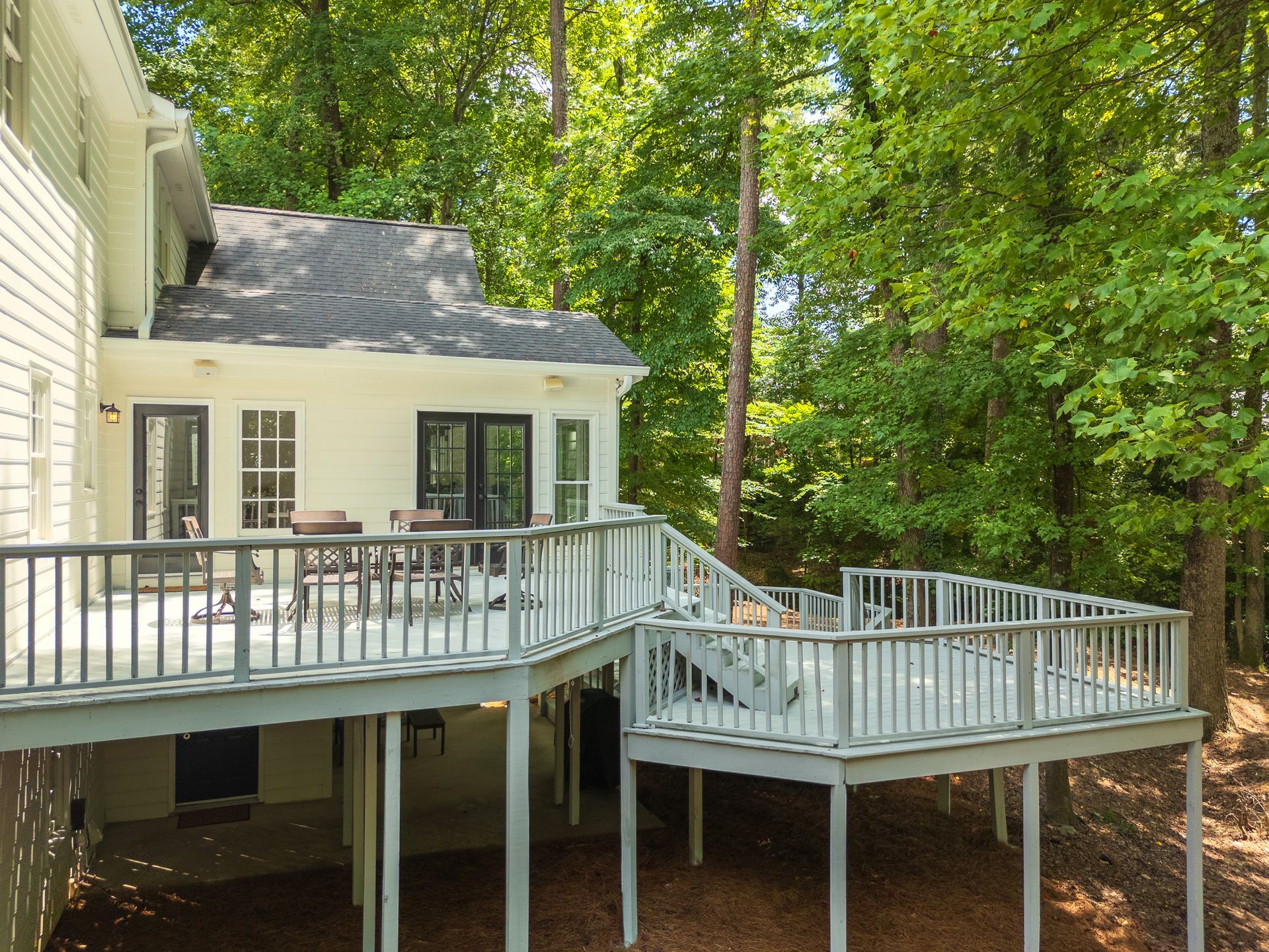 The back of a house with a large deck surrounded by trees.