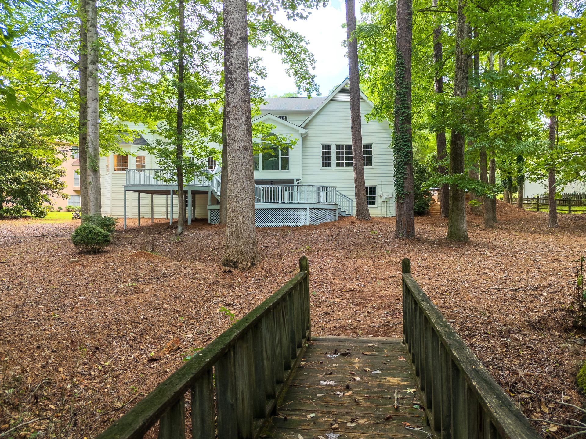 A wooden bridge leads to a house in the woods.