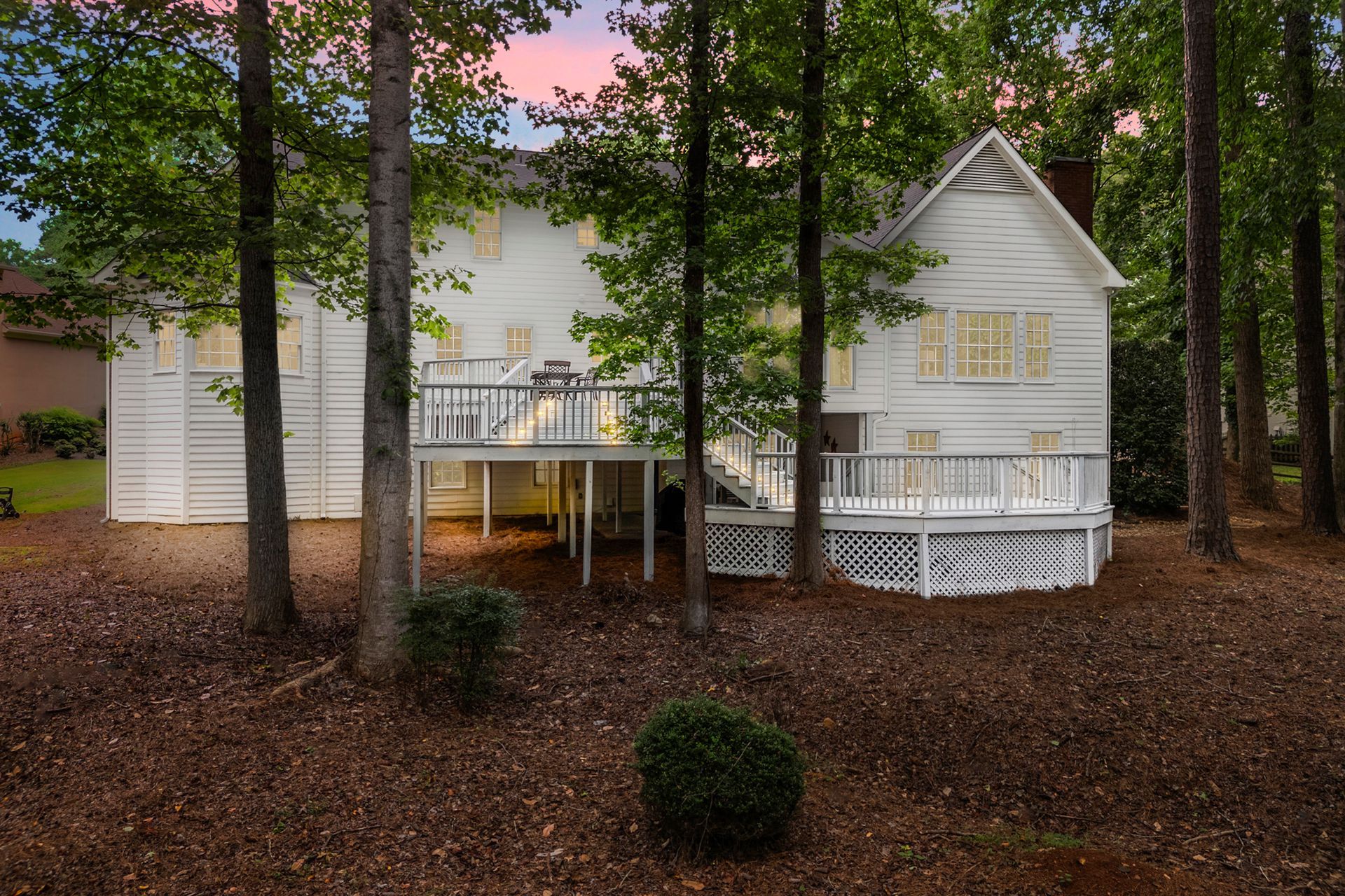 A white house with a large deck is surrounded by trees.