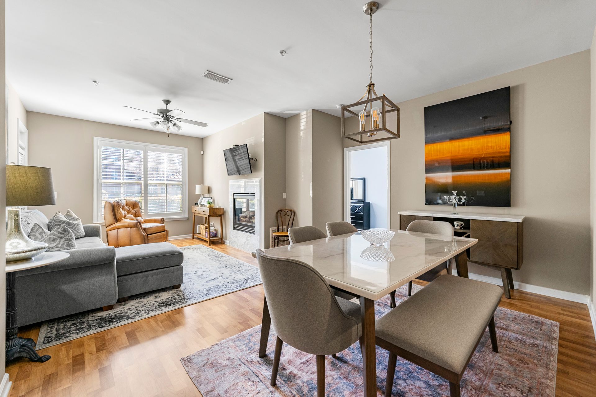 A living room with a dining room table and chairs and a painting on the wall.