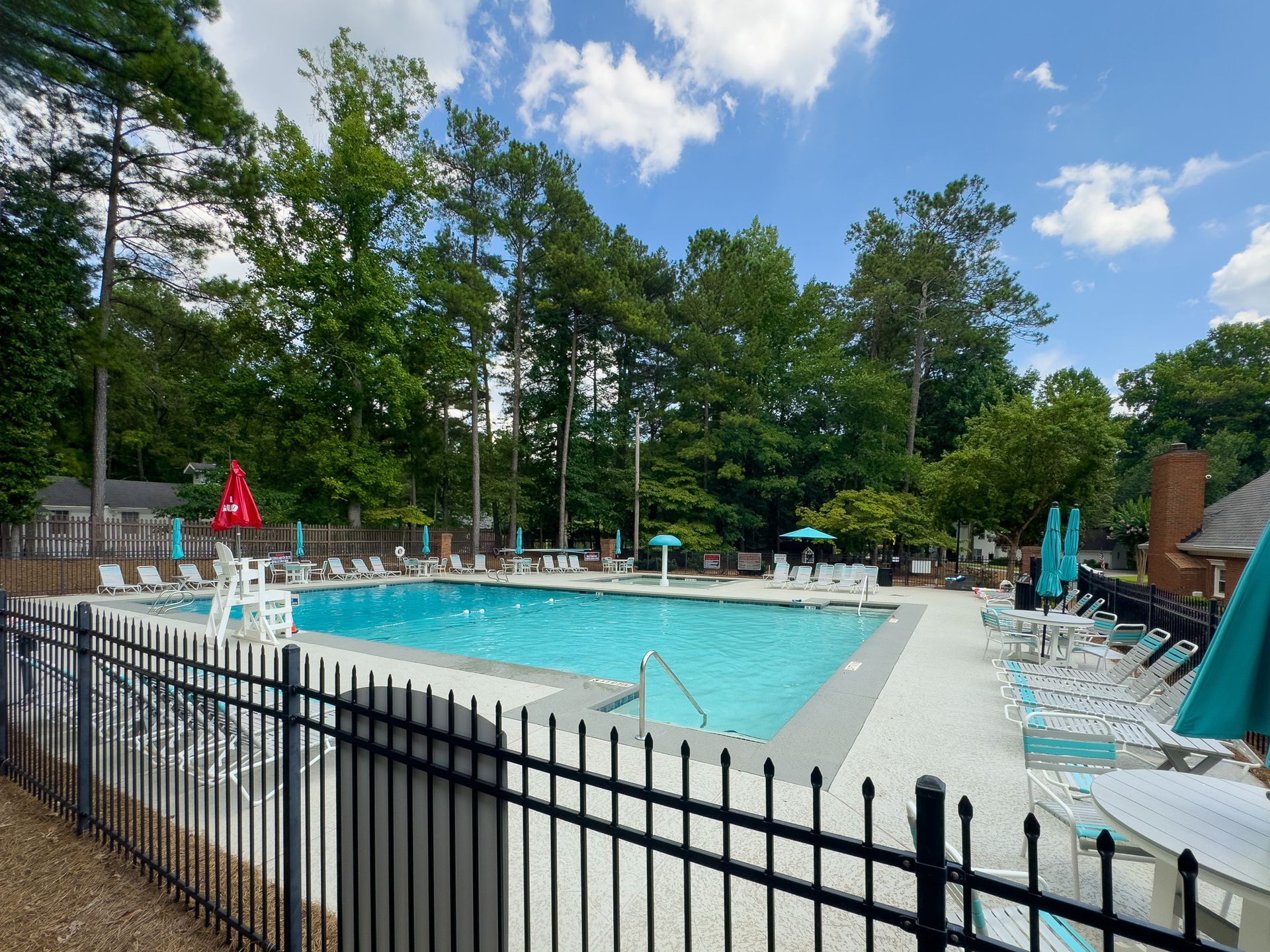 A large swimming pool surrounded by chairs and umbrellas behind a fence.