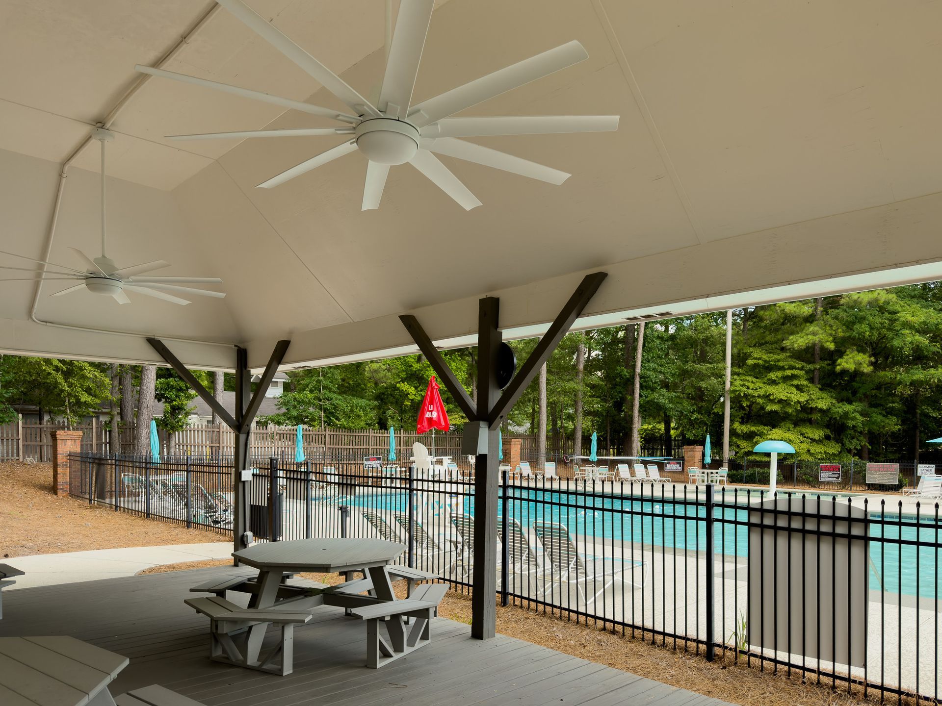 A picnic table under a ceiling fan next to a pool