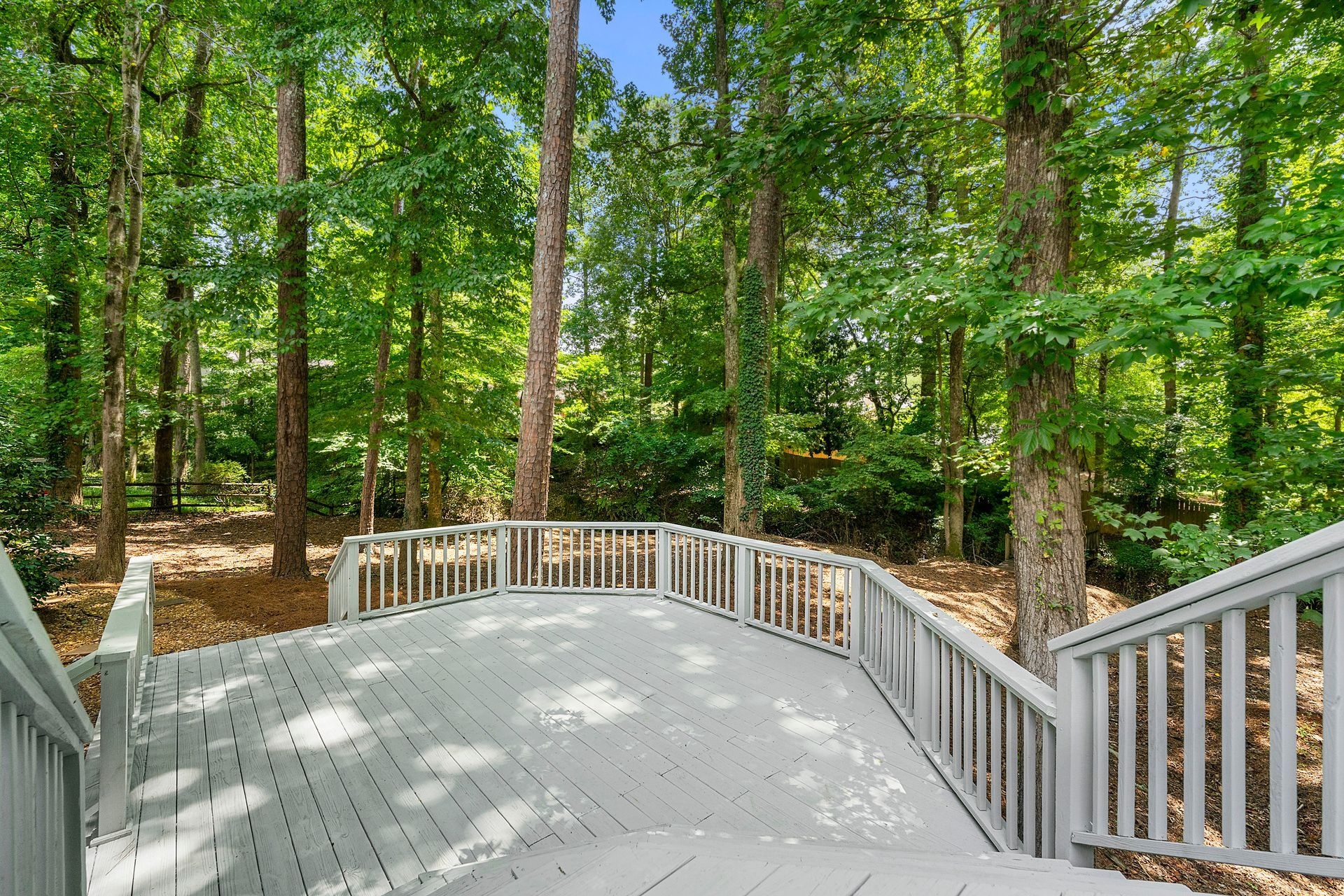 A large deck with a railing in the middle of a forest.