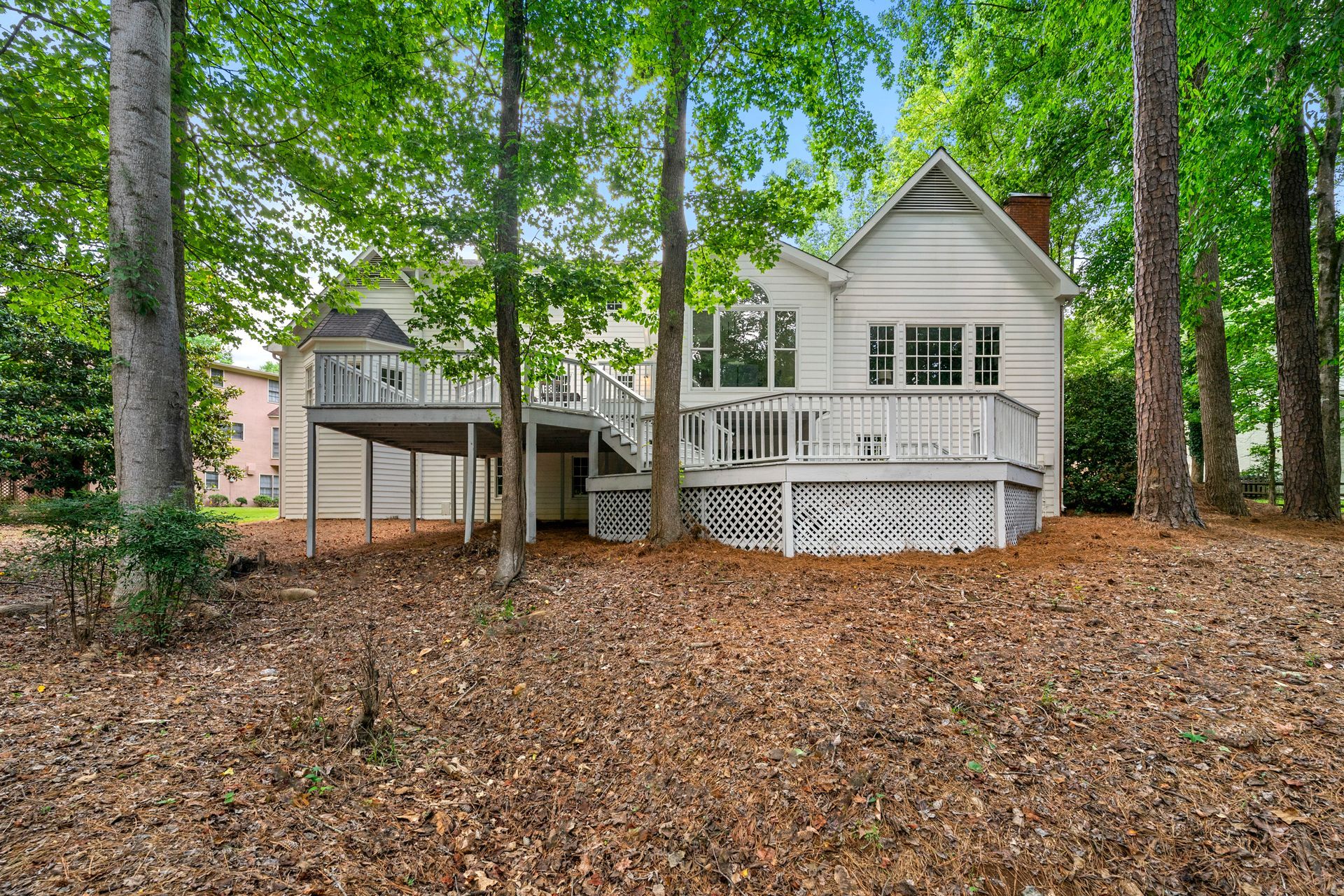 A white house with a large deck is surrounded by trees.