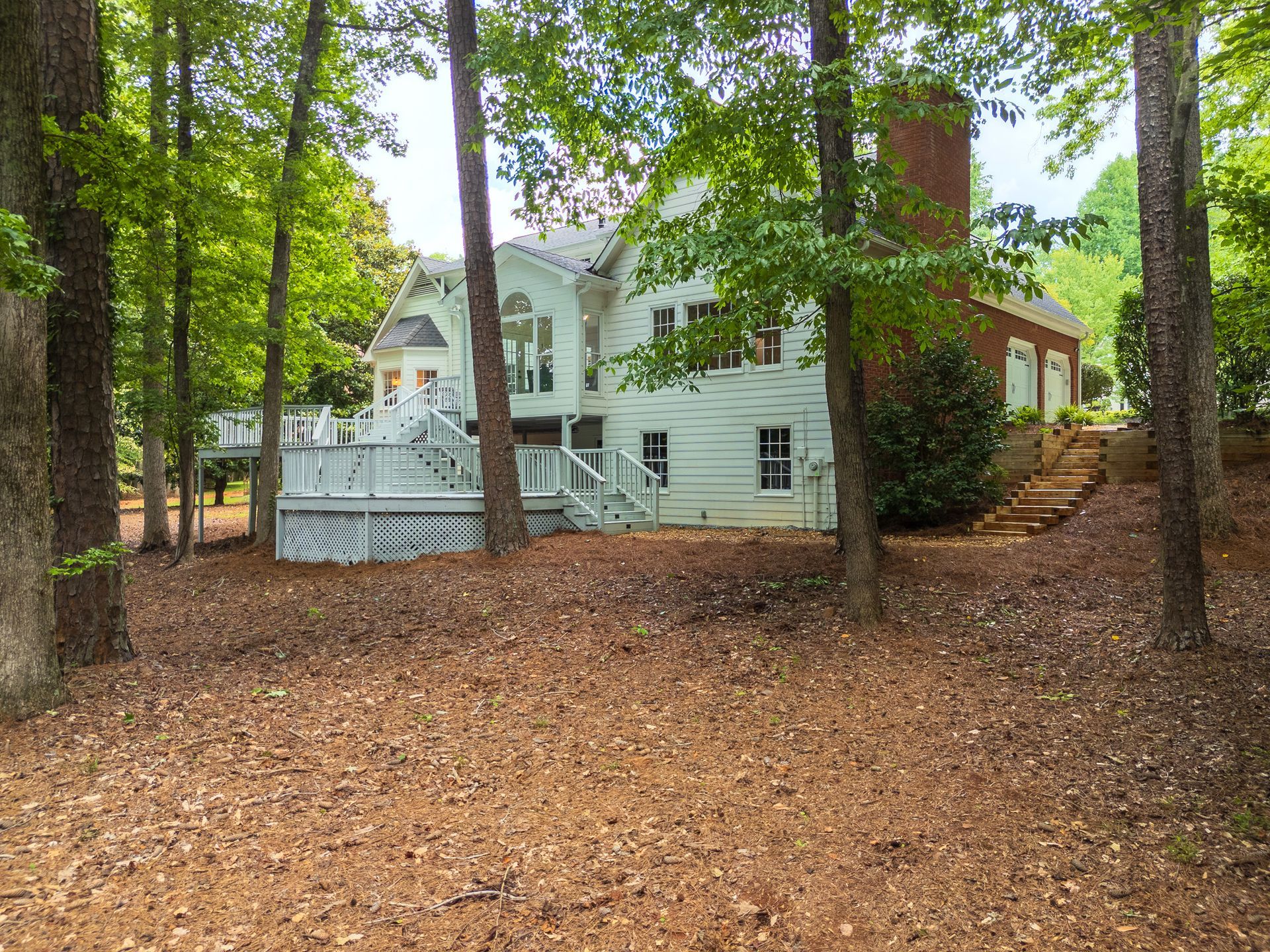 A large white house is surrounded by trees and leaves.