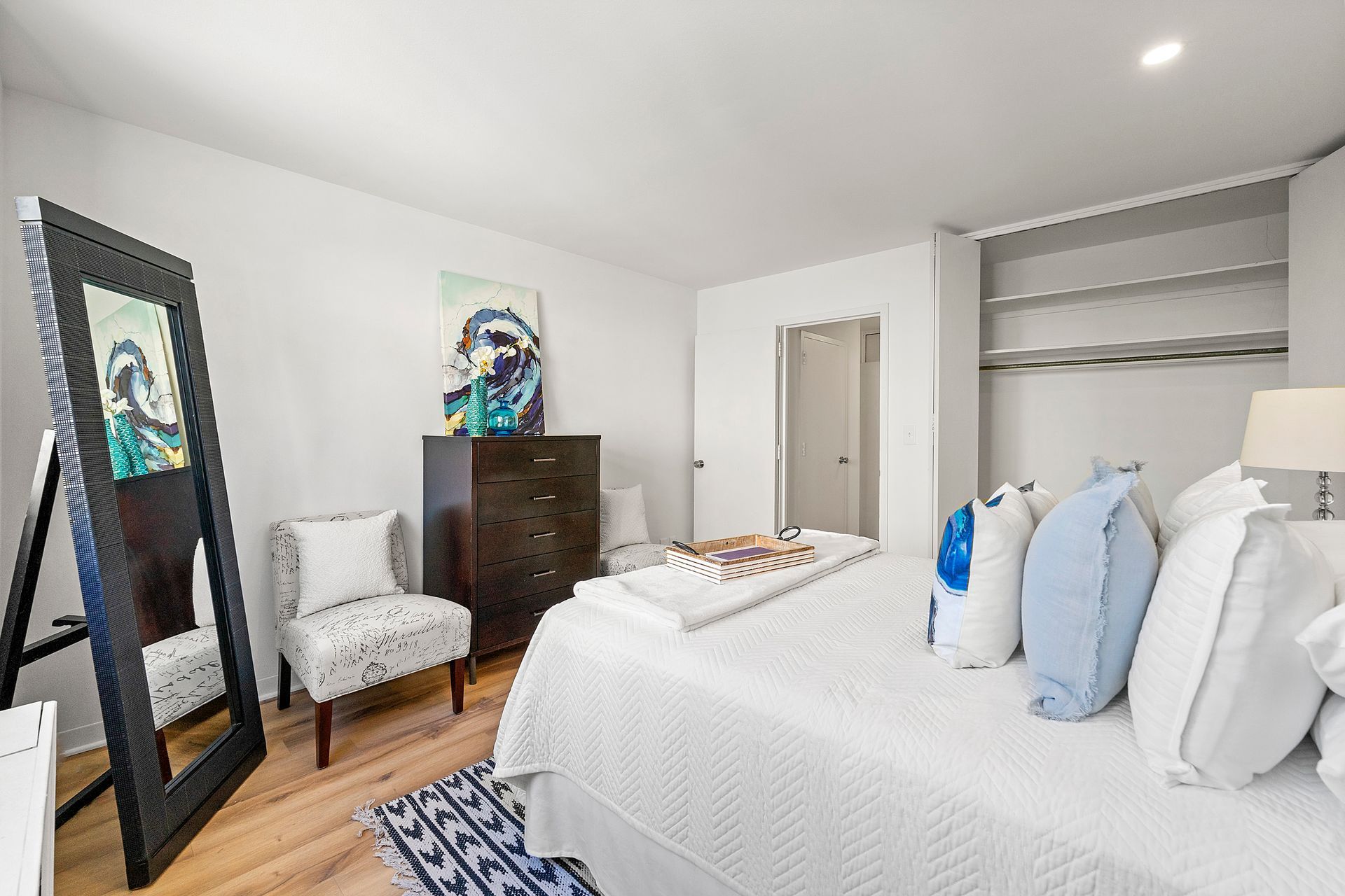 A bedroom with a large bed , dresser , chair and mirror.
