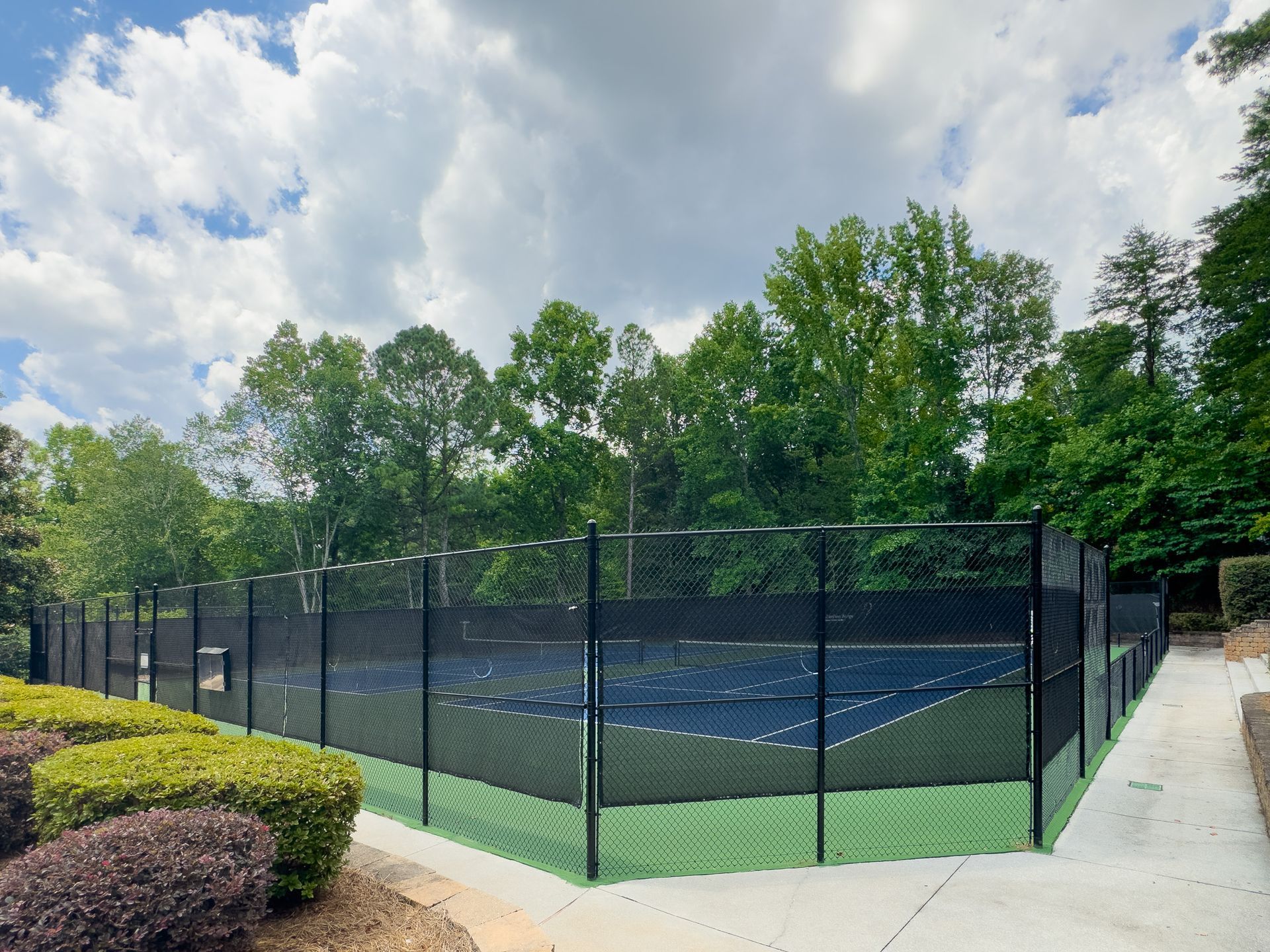 A tennis court with a fence around it and trees in the background