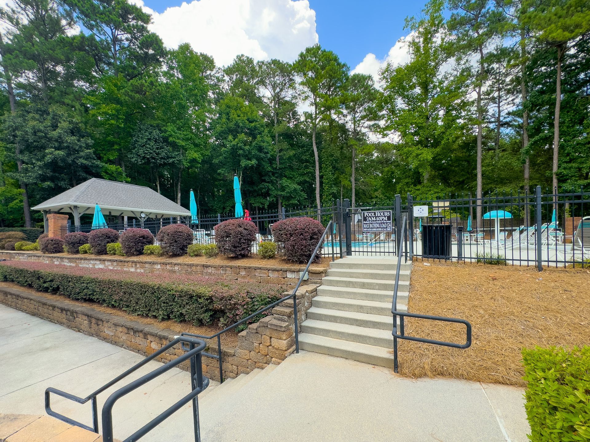 A swimming pool with a pavilion and stairs leading to it surrounded by trees.