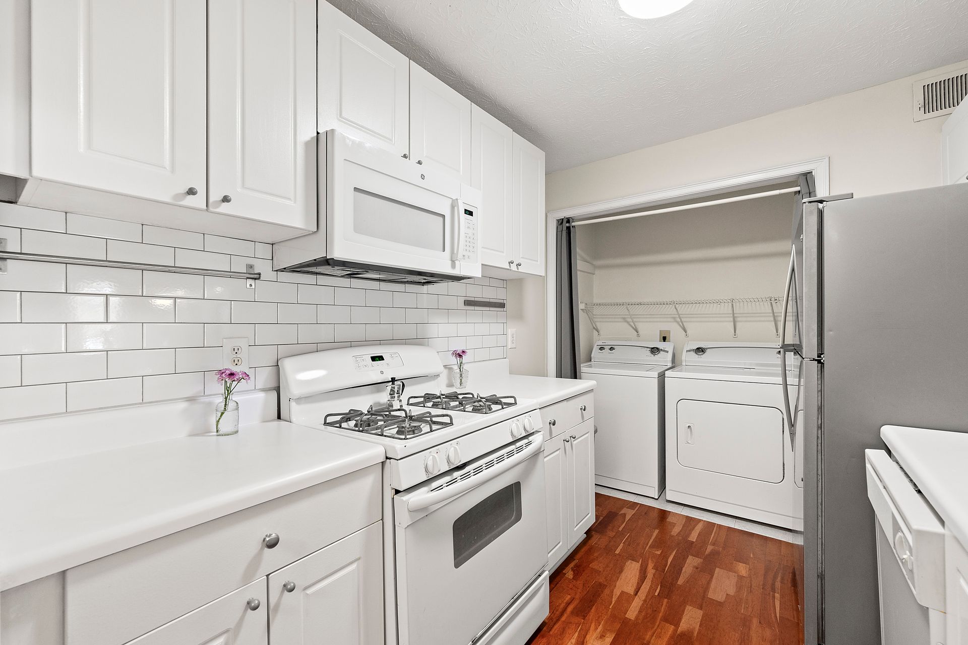 A kitchen with white cabinets , a stove , a refrigerator , and a microwave.