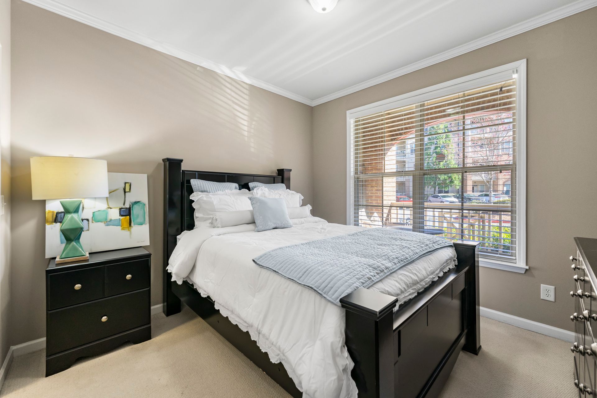 A bedroom with a bed , nightstand , lamp and window.