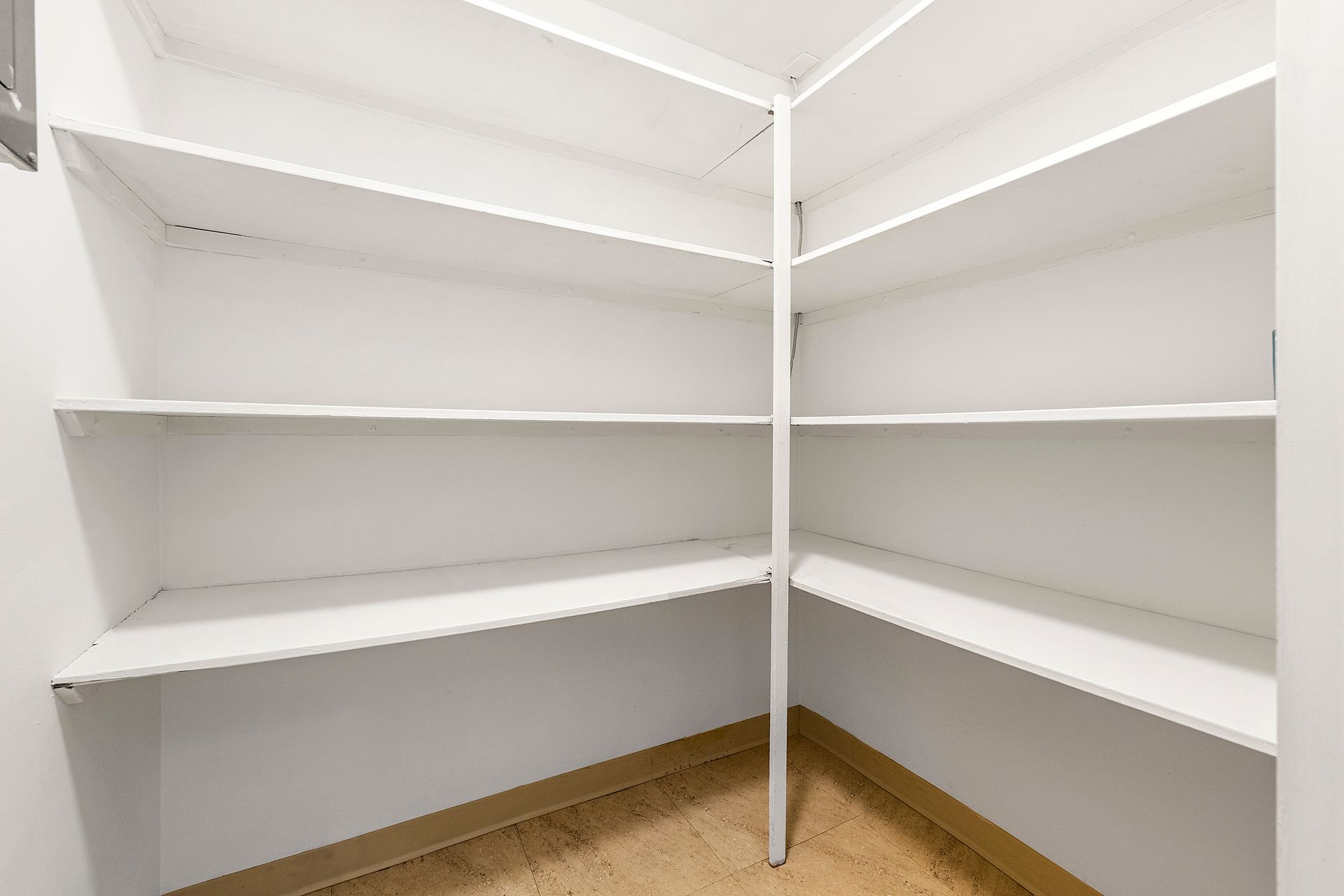 An empty walk in closet with white shelves and a wooden floor.