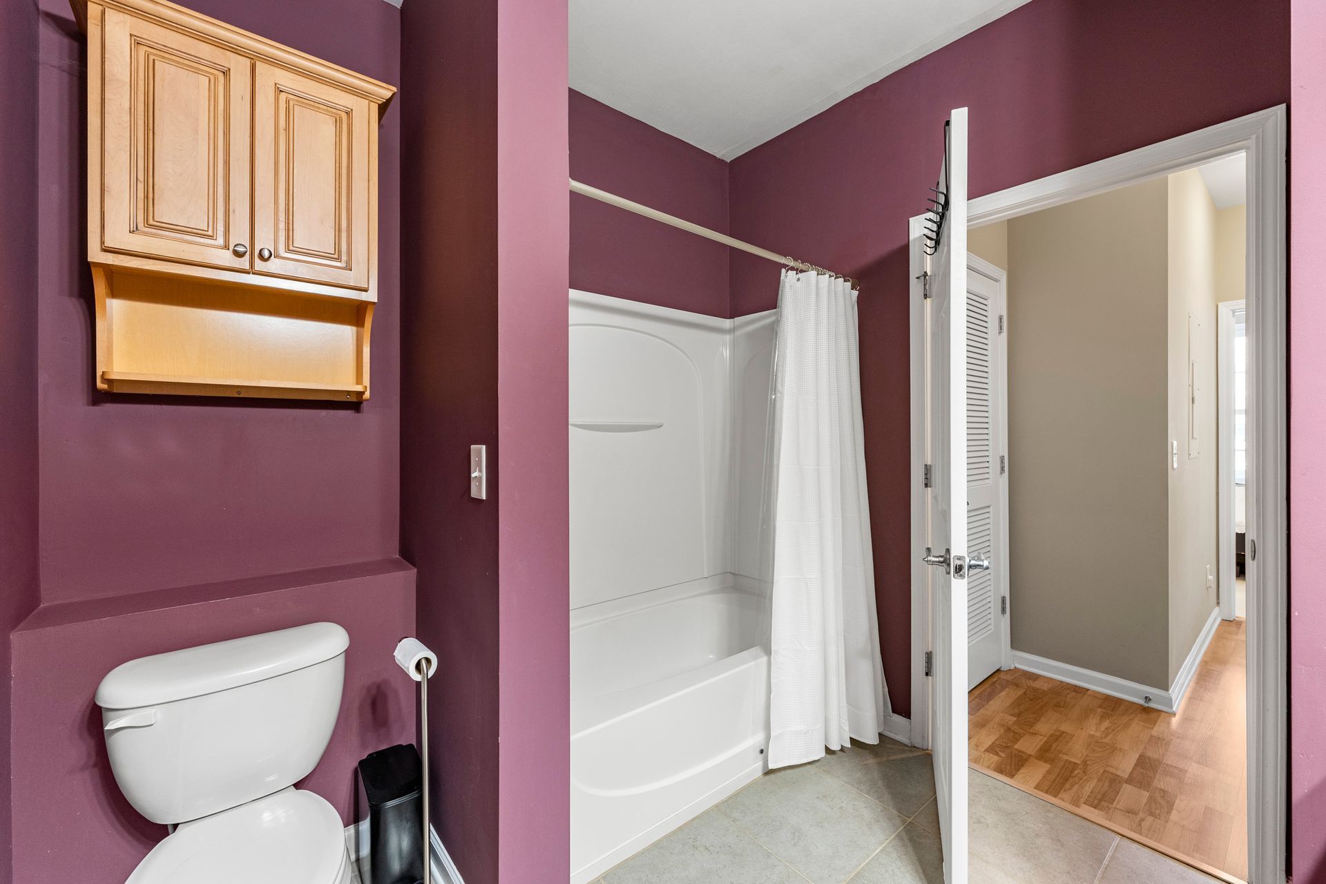 A bathroom with purple walls , a toilet , and a bathtub.