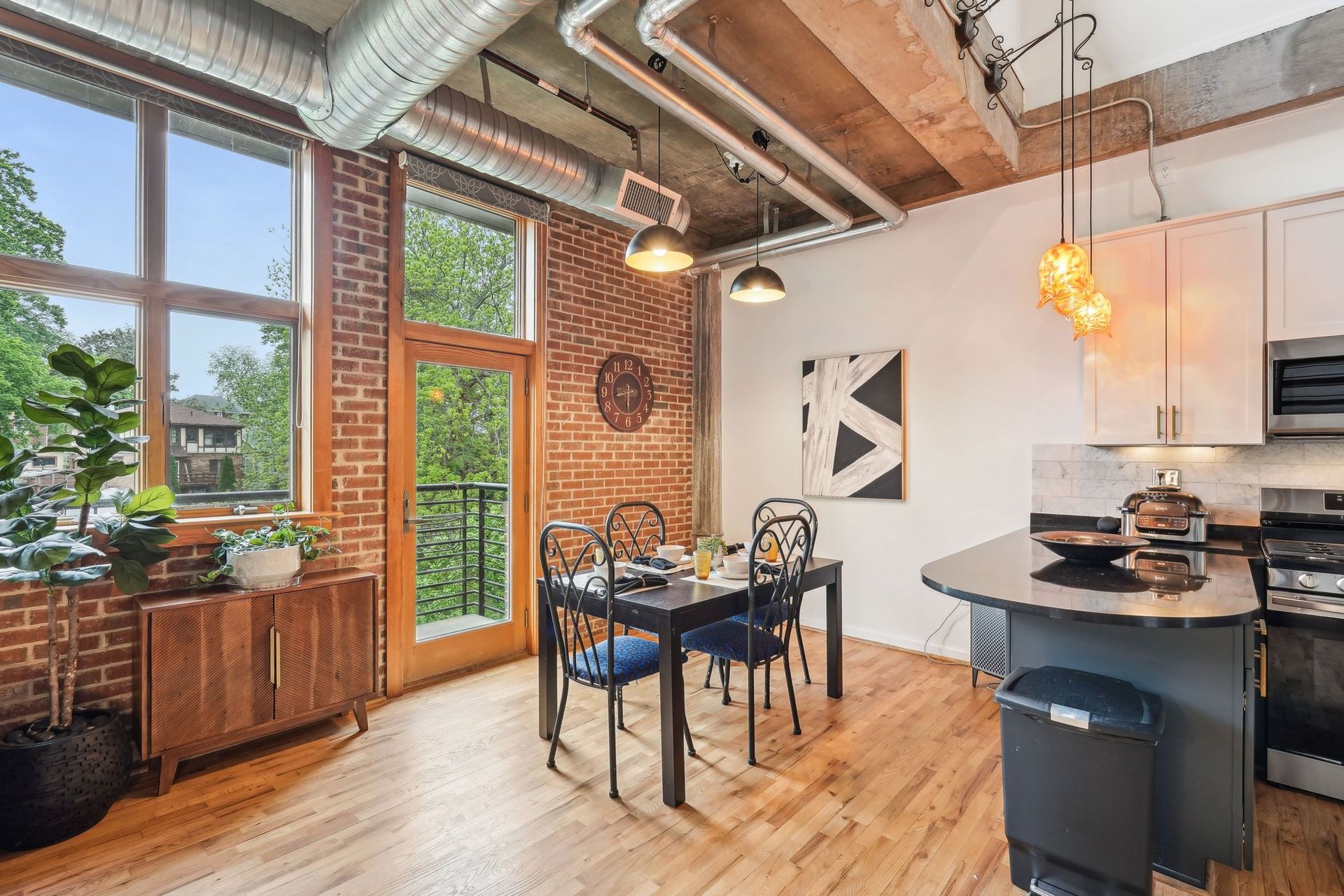 Dining area with exposed brick and ductwork, wood floor, small balcony.