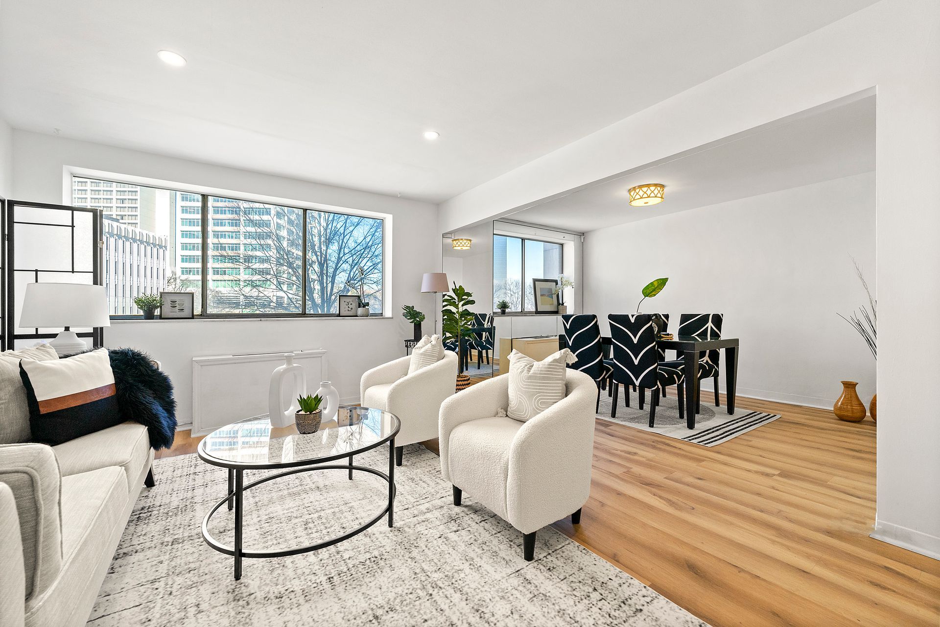 A living room with a couch , chairs , a coffee table and a large window.