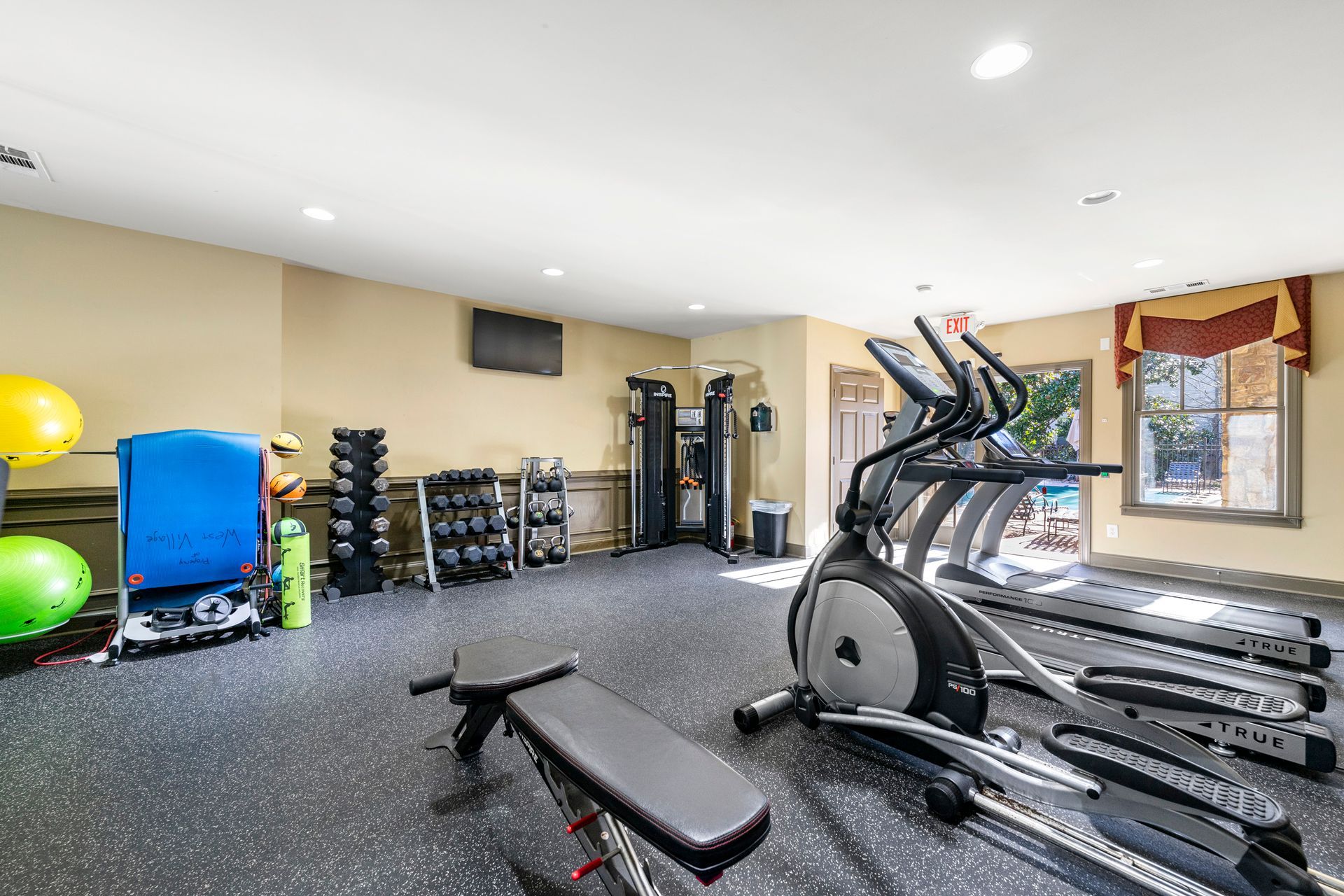 A gym with a treadmill , elliptical , and bench.