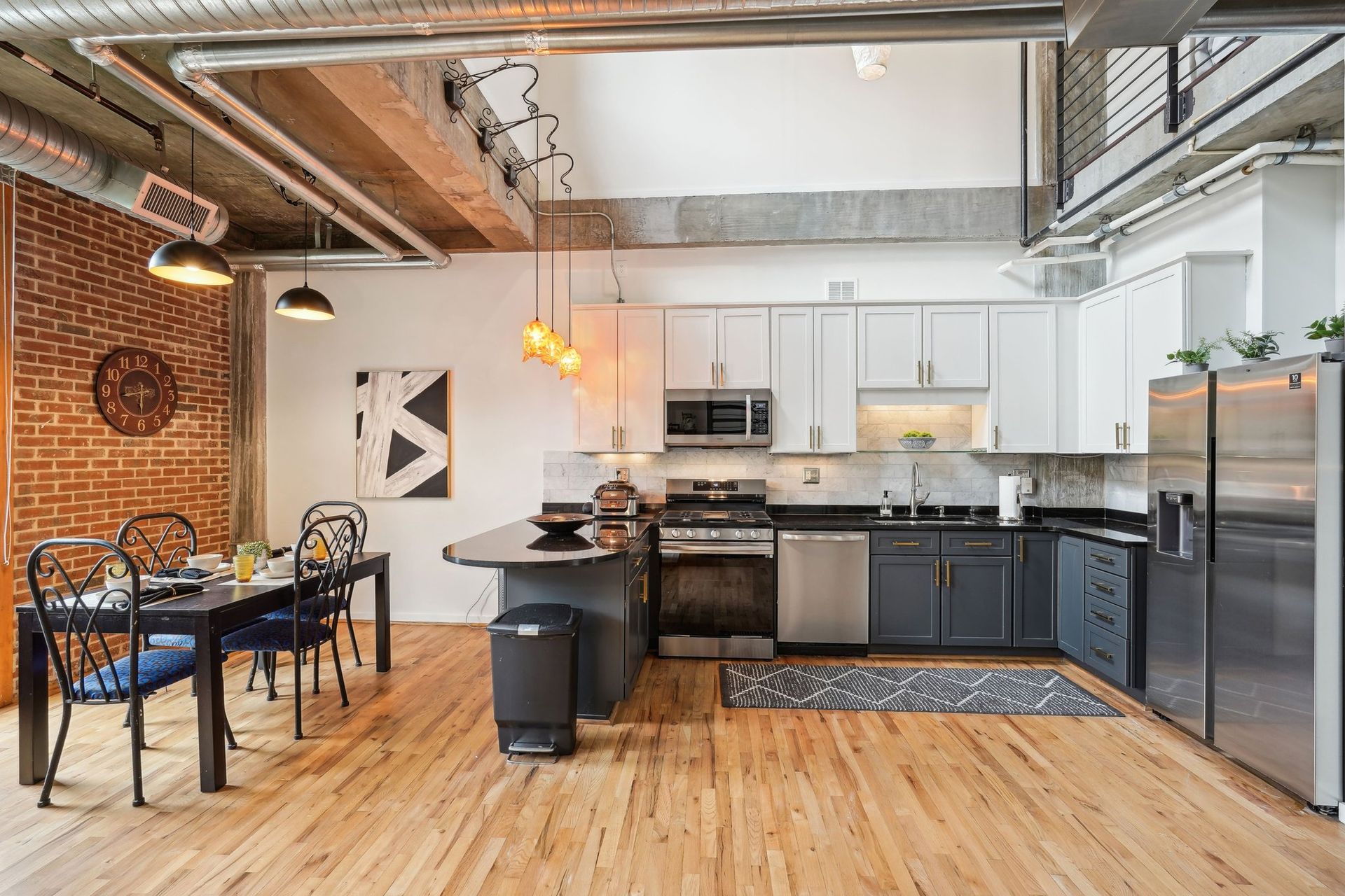 Modern kitchen with wooden floors, brick wall, and stainless steel appliances.