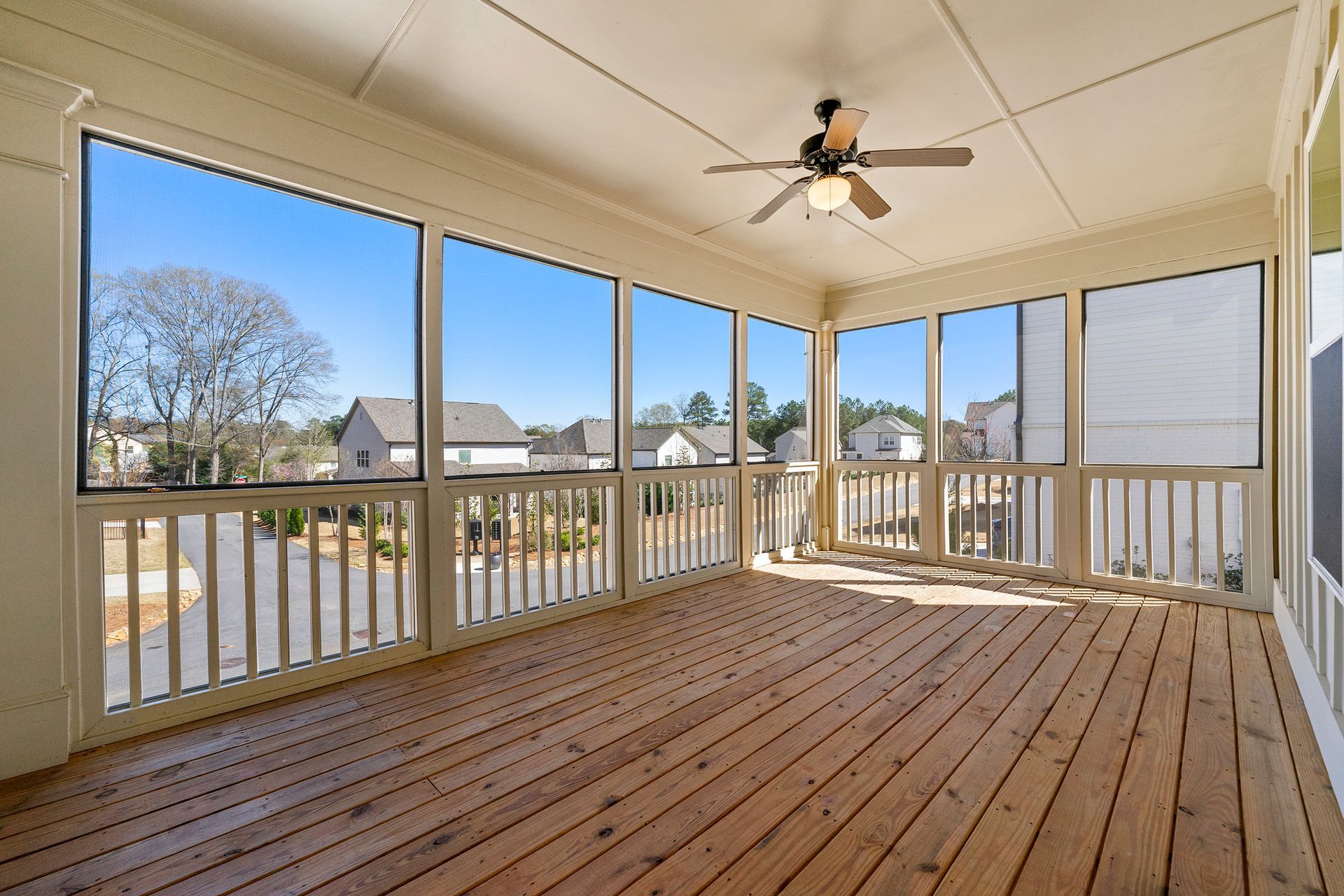 An empty screened in porch with a ceiling fan