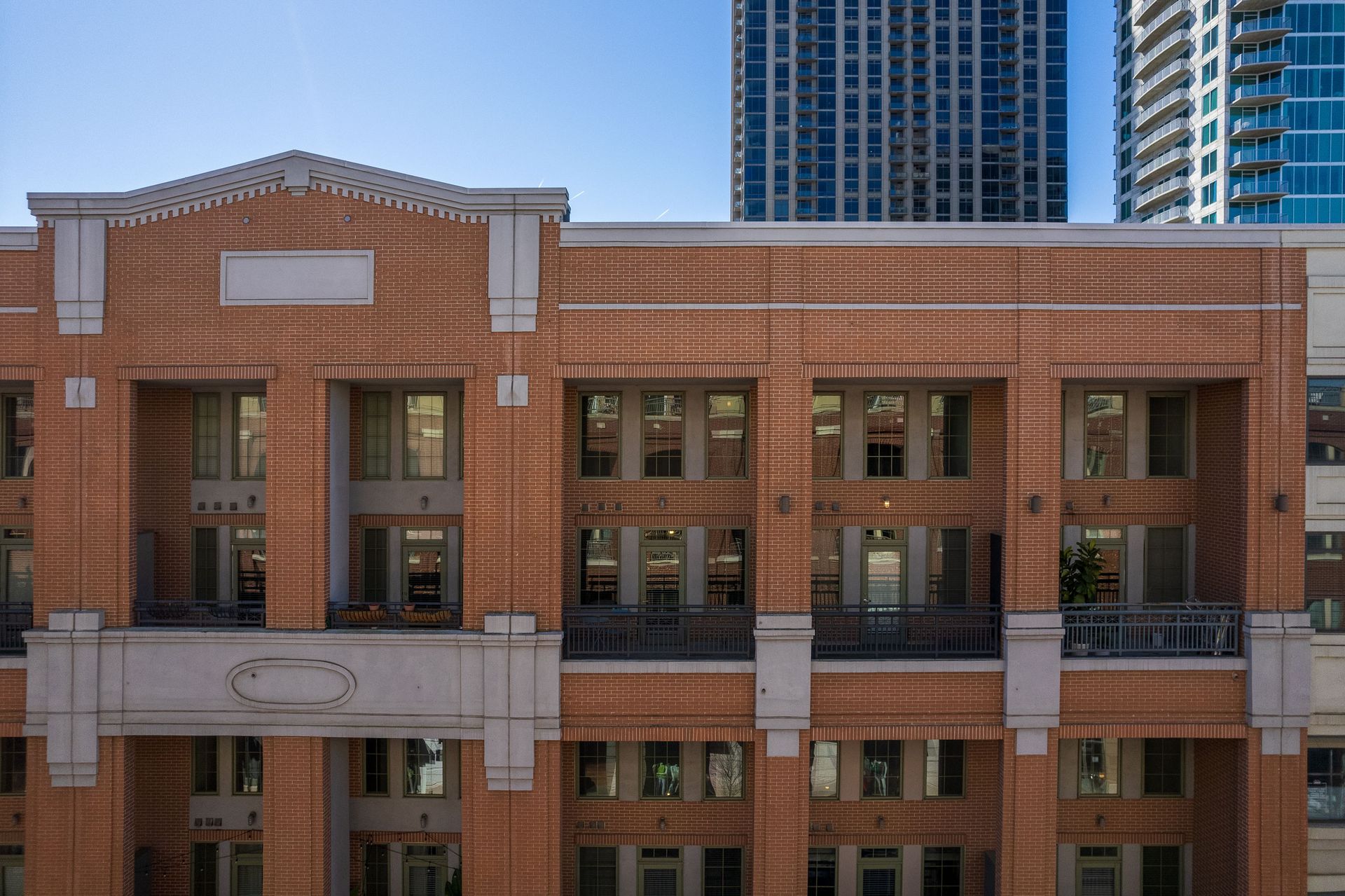 A large brick building with a balcony and a skyscraper in the background.