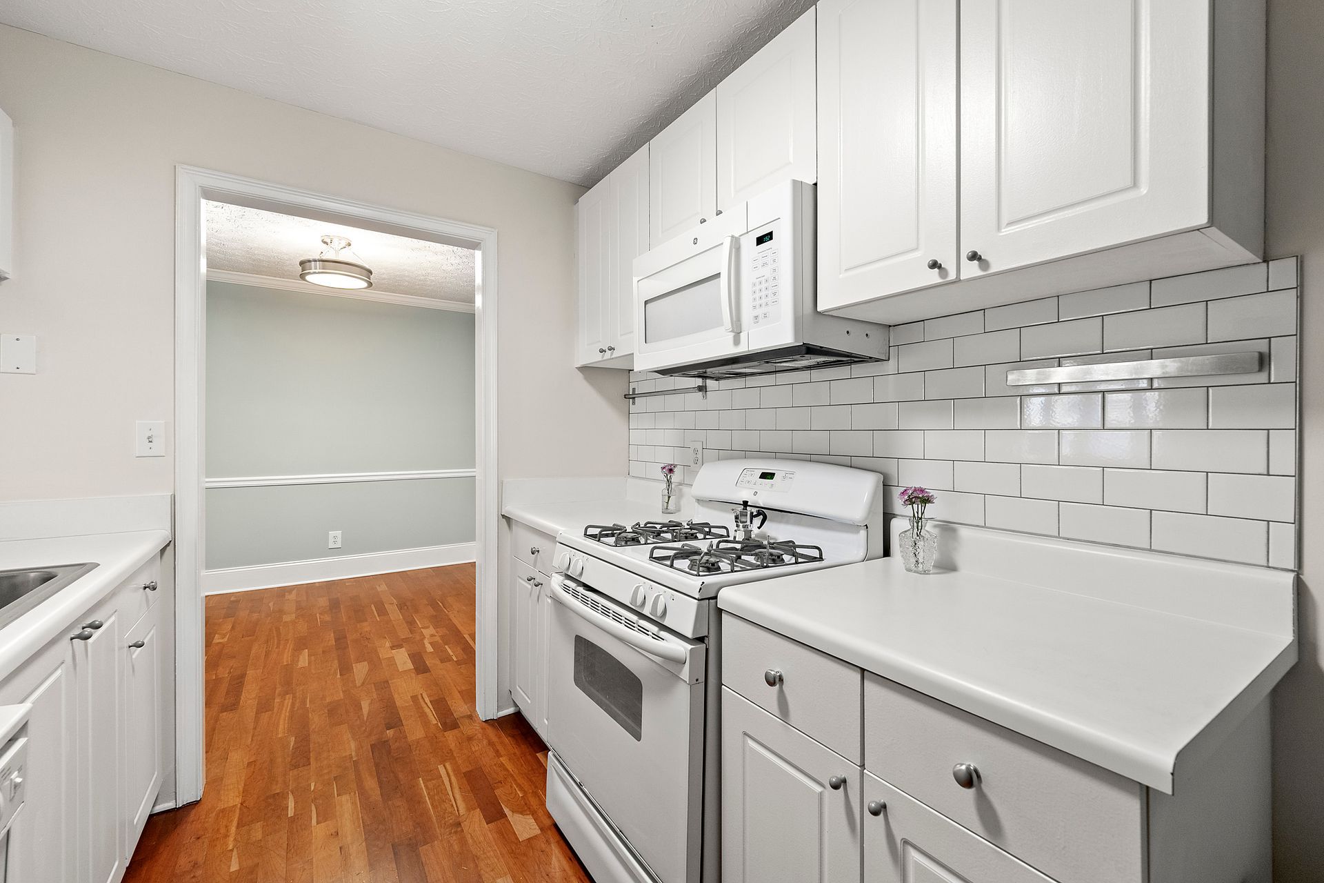 A kitchen with white cabinets , a stove , a microwave and a sink.