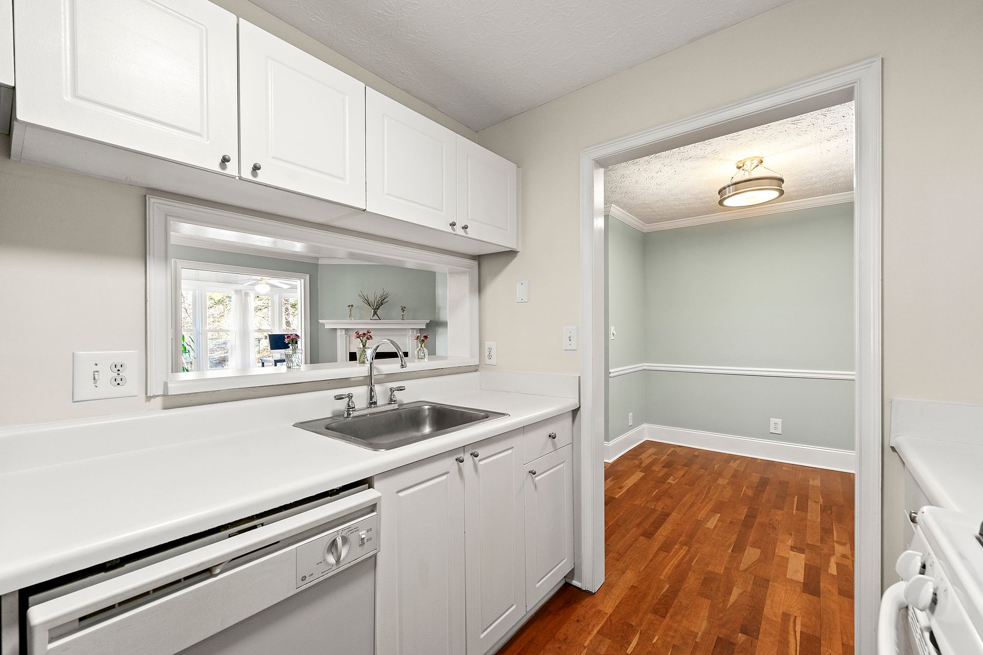 A kitchen with white cabinets , a sink , a dishwasher and a window.