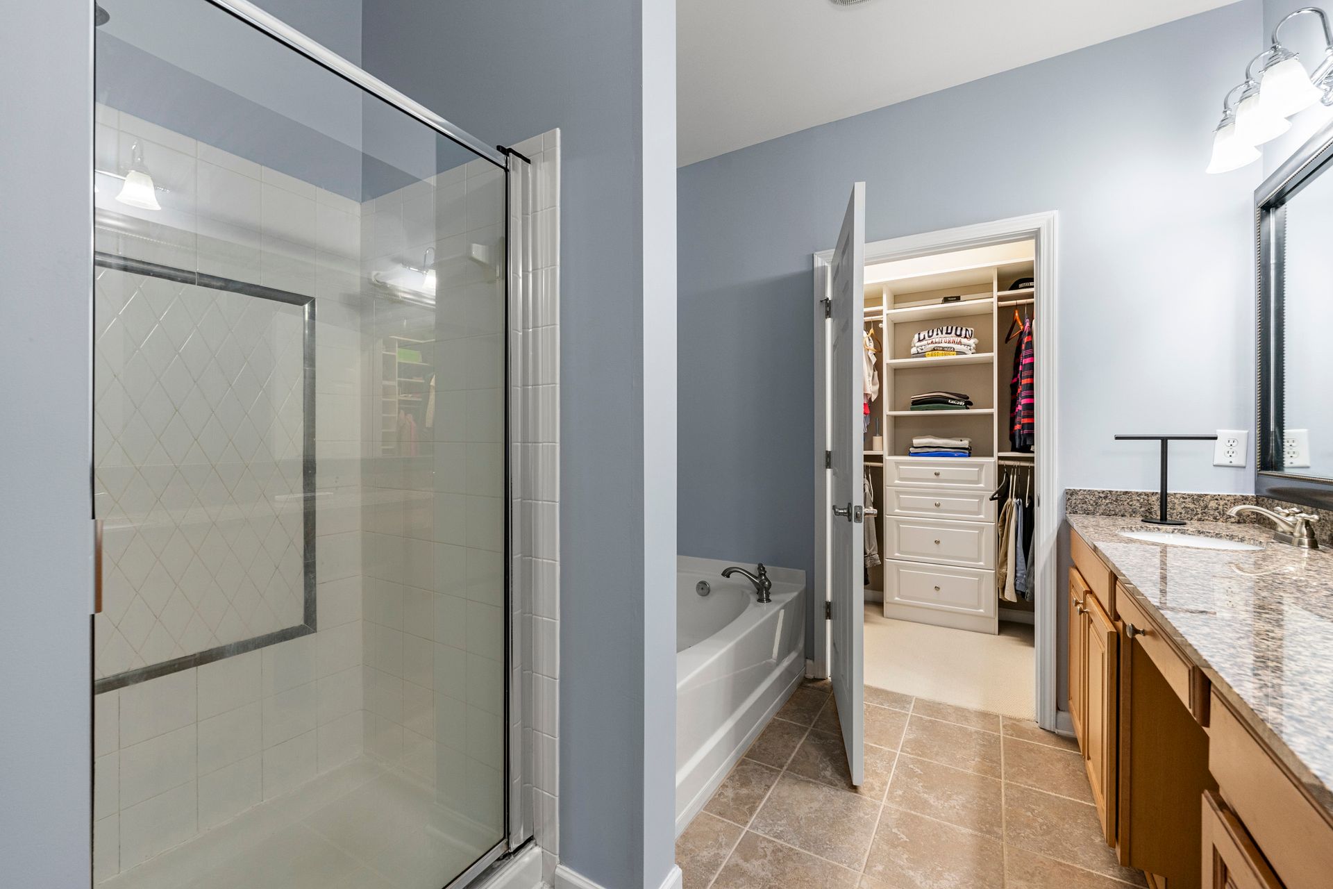 A bathroom with a walk in closet , tub , sink and shower.