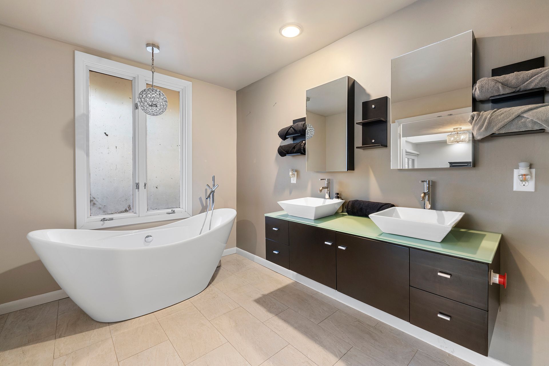 A bathroom with two sinks , a tub and a window.