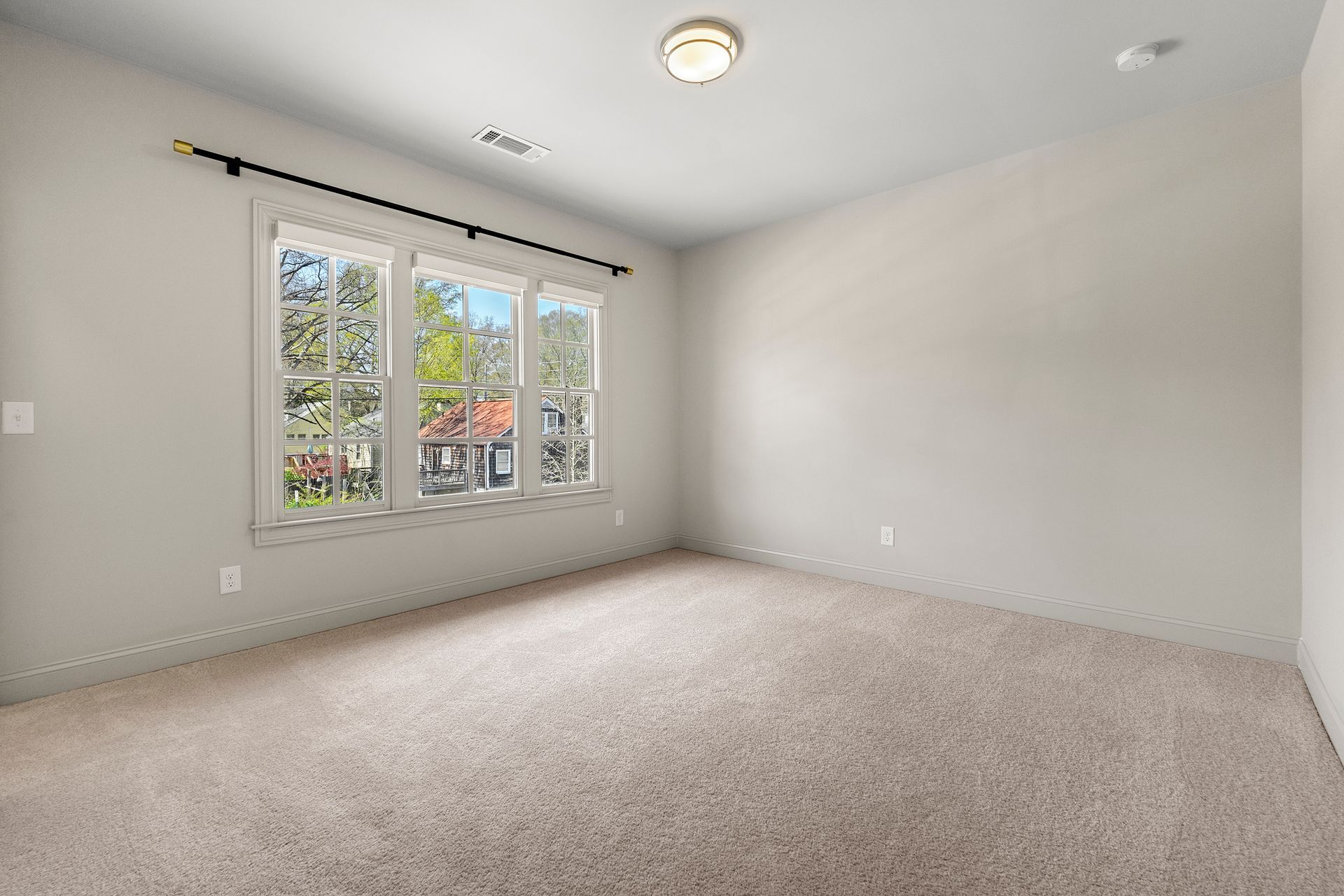 An empty bedroom with a carpeted floor and three windows.