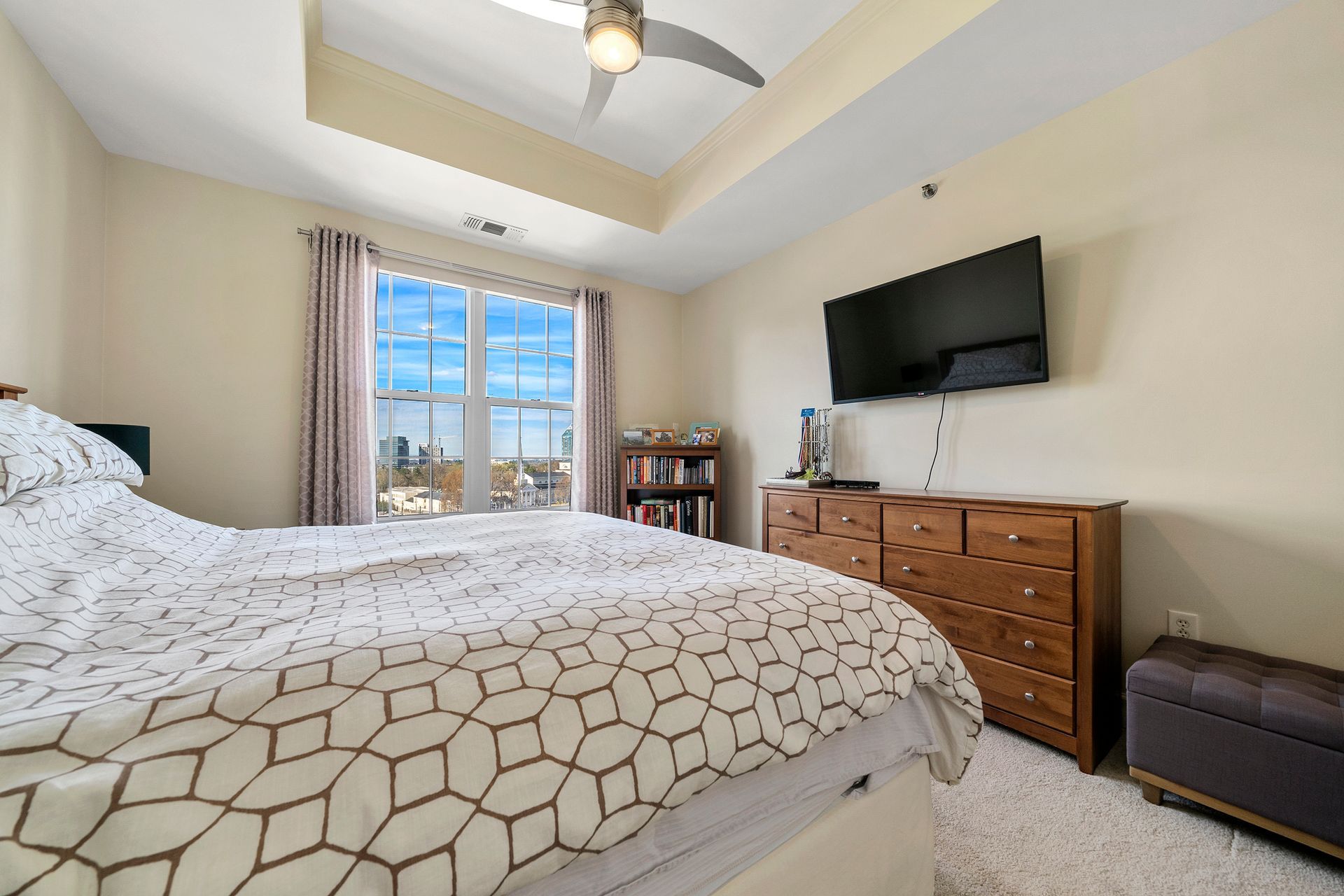 A bedroom with a bed , dresser , television and ceiling fan.