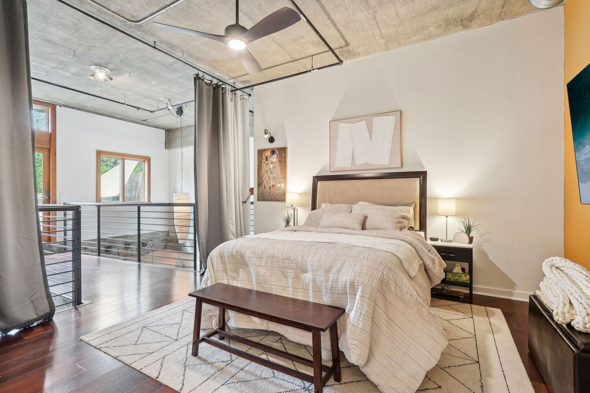 Bedroom with bed, bench, rug, neutral colors, and loft overlooking a balcony.