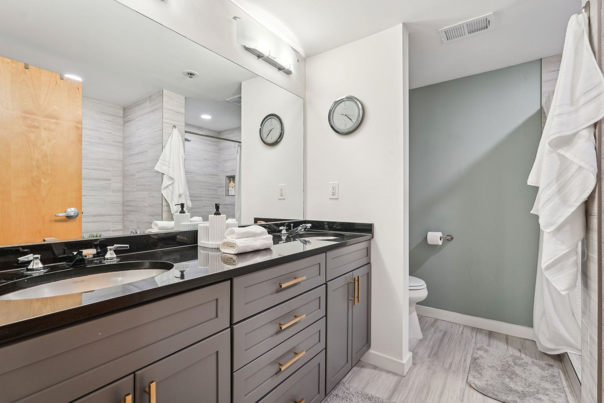 Bathroom with gray cabinets, black countertop, large mirror, and pale blue-green wall.