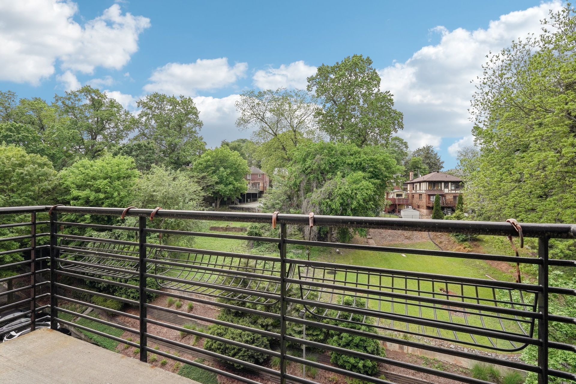Balcony view of lush greenery, blue sky with clouds, and distant buildings.