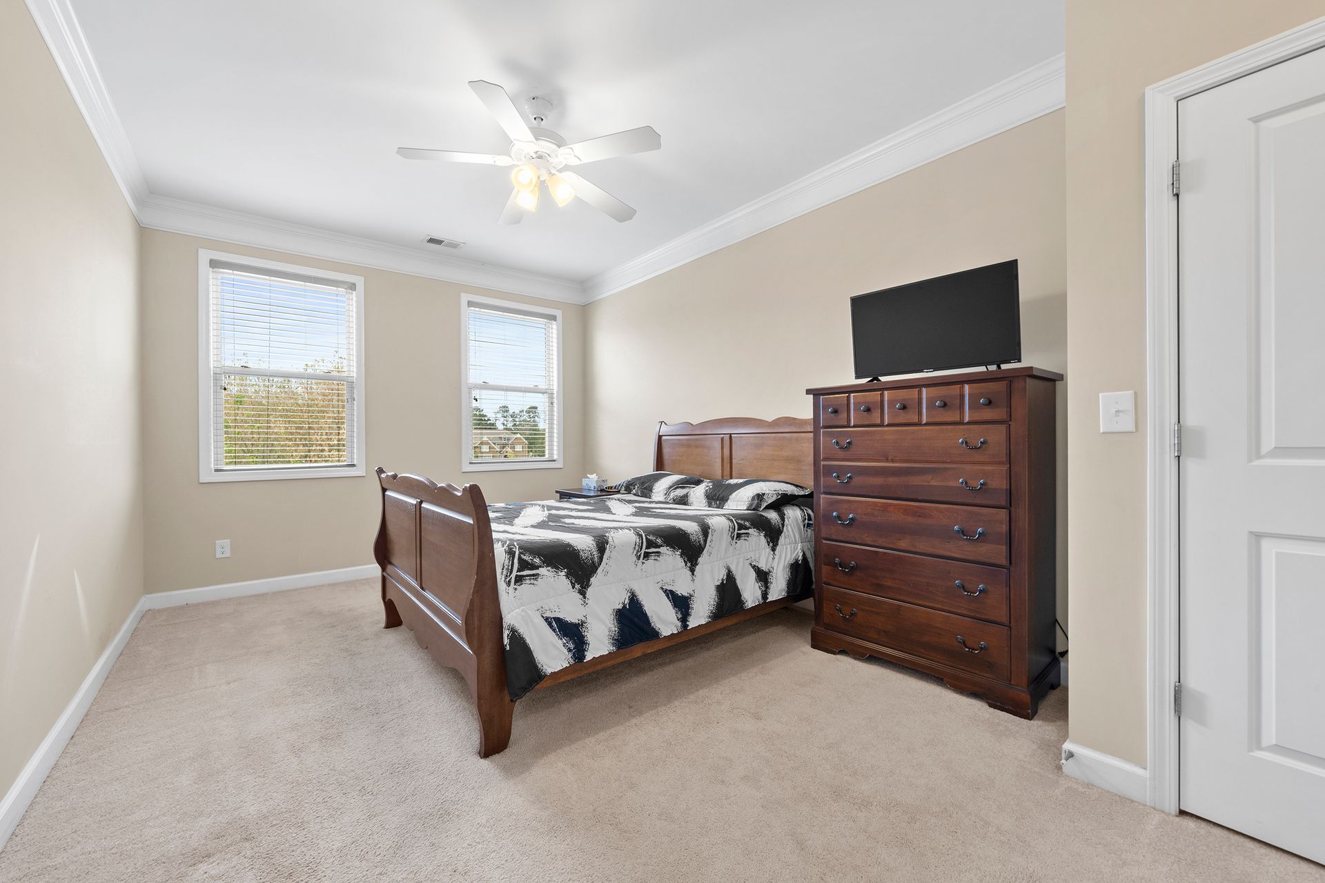 A bedroom with a bed , dresser , television and ceiling fan.